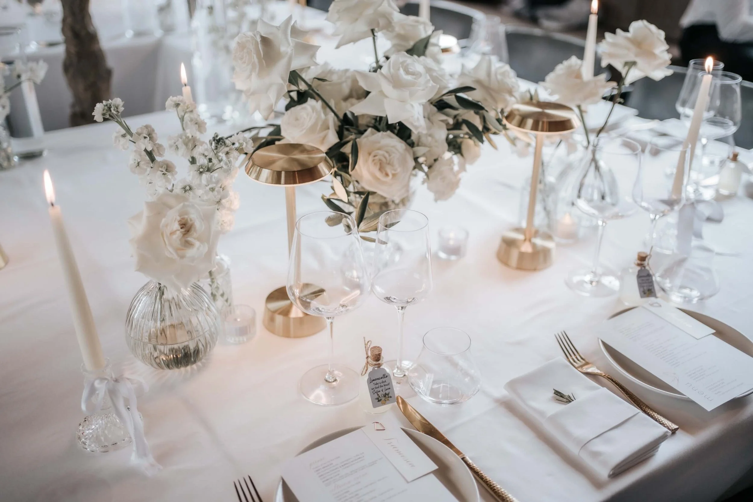 Elegant dining table decorated with white flowers, candles, and gold accents for a formal event or wedding reception.