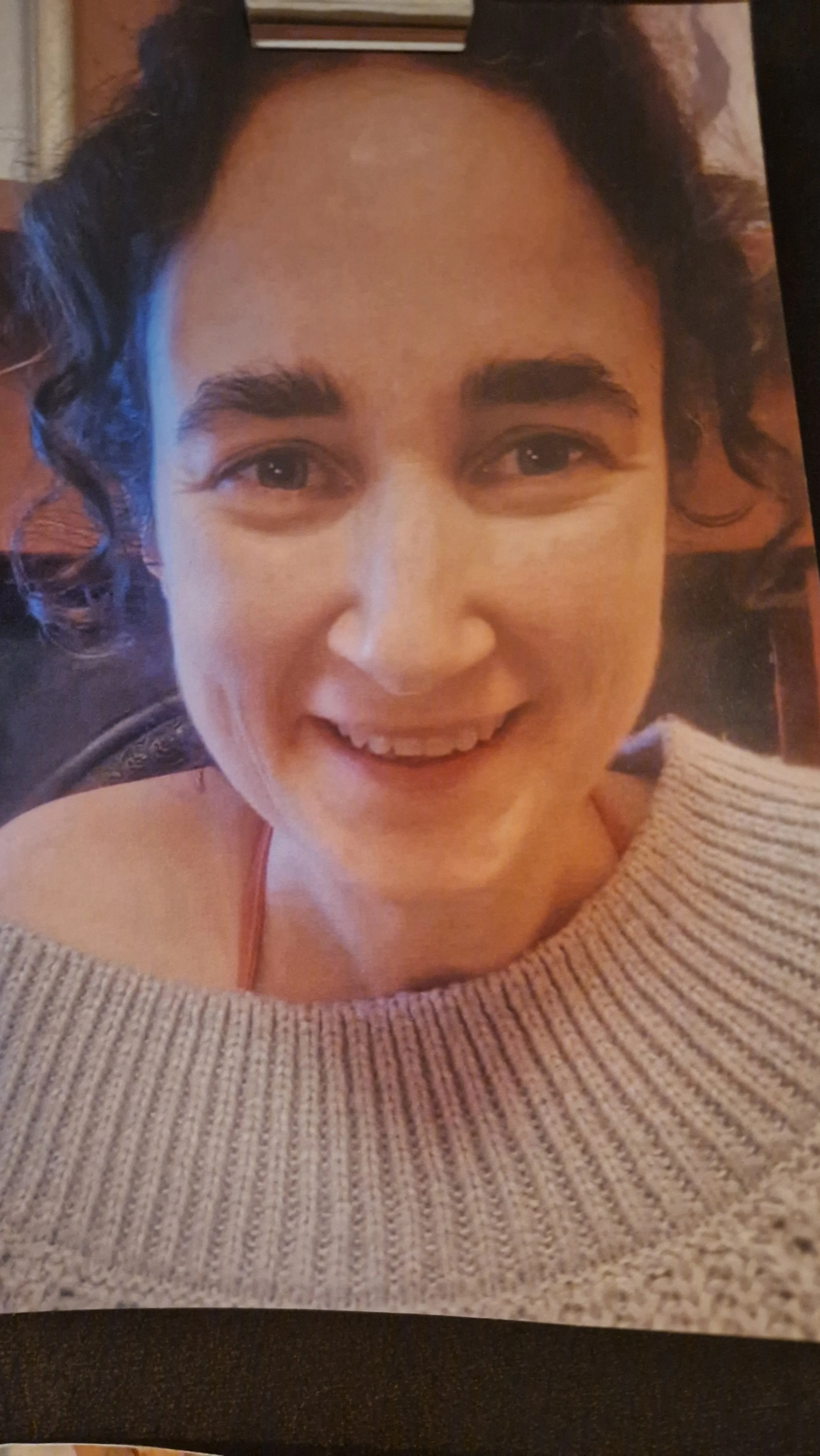 Close-up of a woman with curly dark hair, smiling, wearing a beige knit jumper.