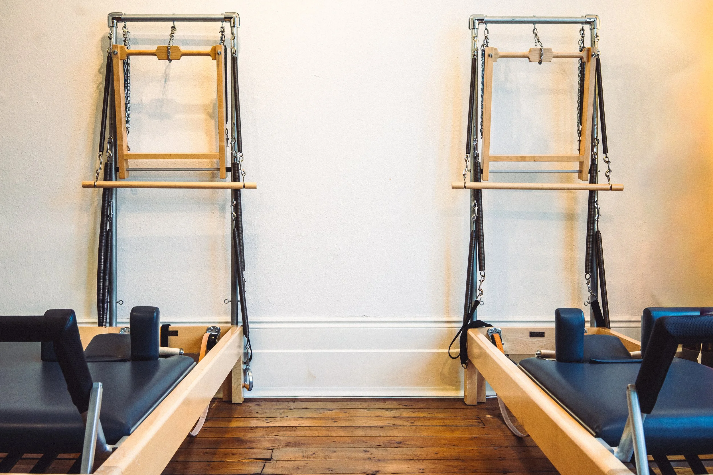 2 reformers are arranged in a warmly lit Pilates studio