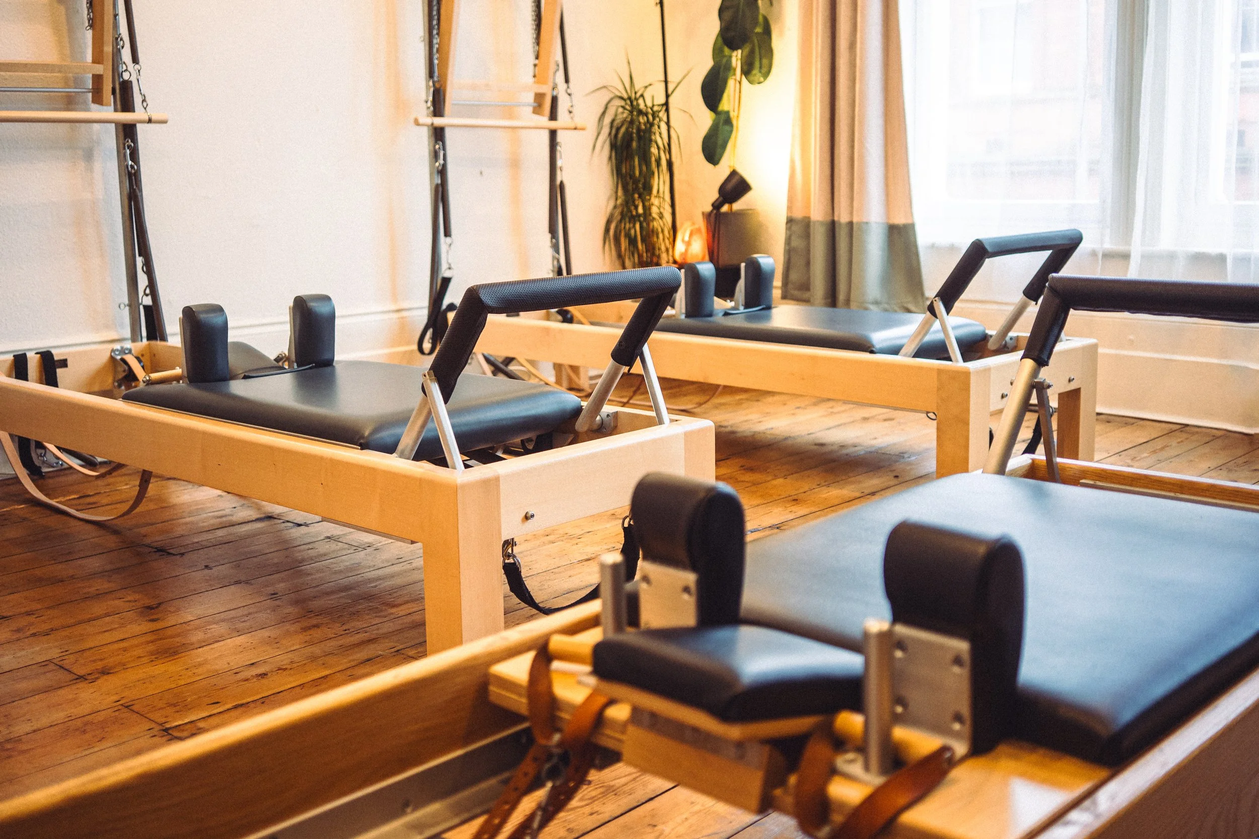 3 reformers are arranged in a warmly lit Pilates studio