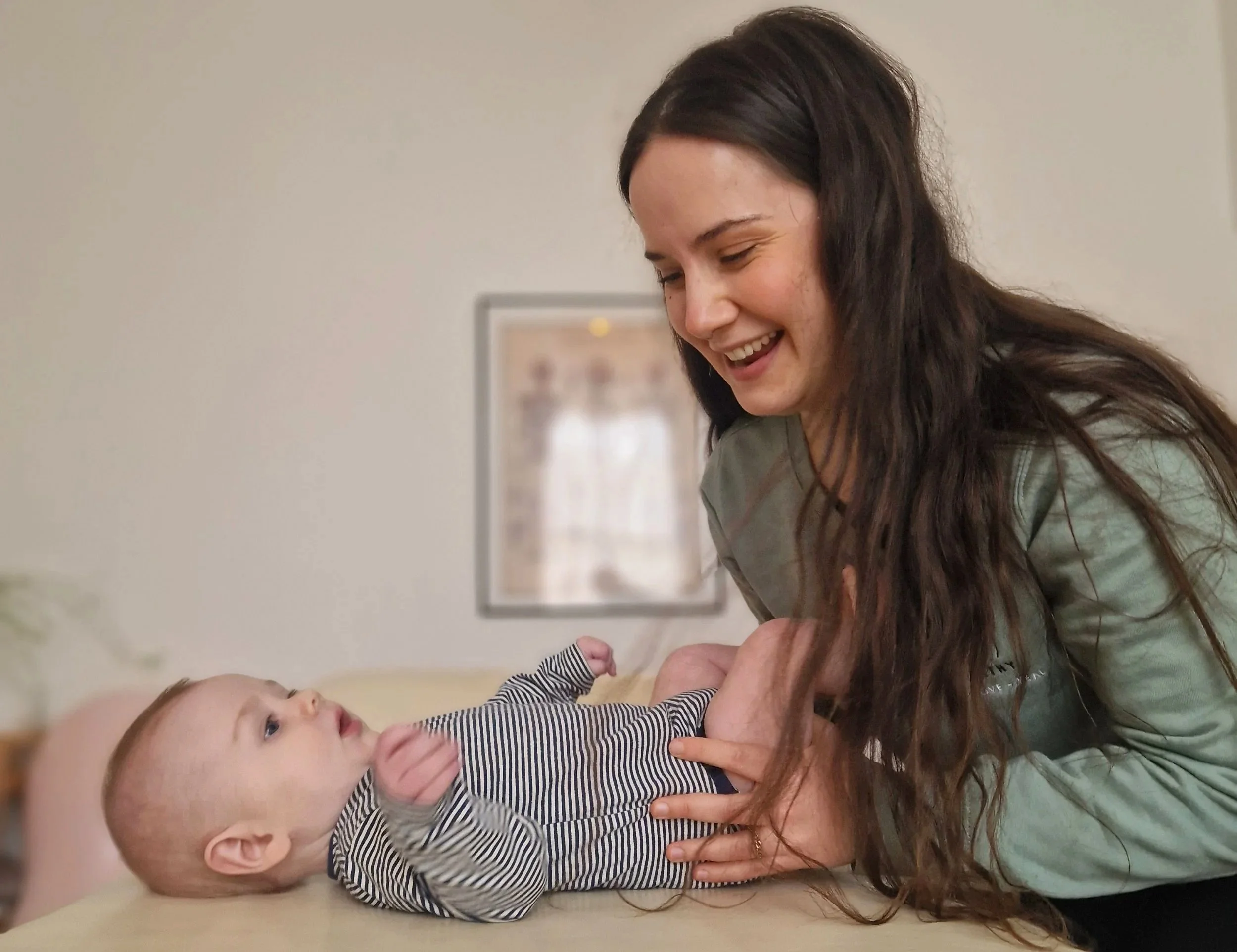 A female Osteopath giving a baby a treatment on a treatment couch in a room with framed art on the wall.