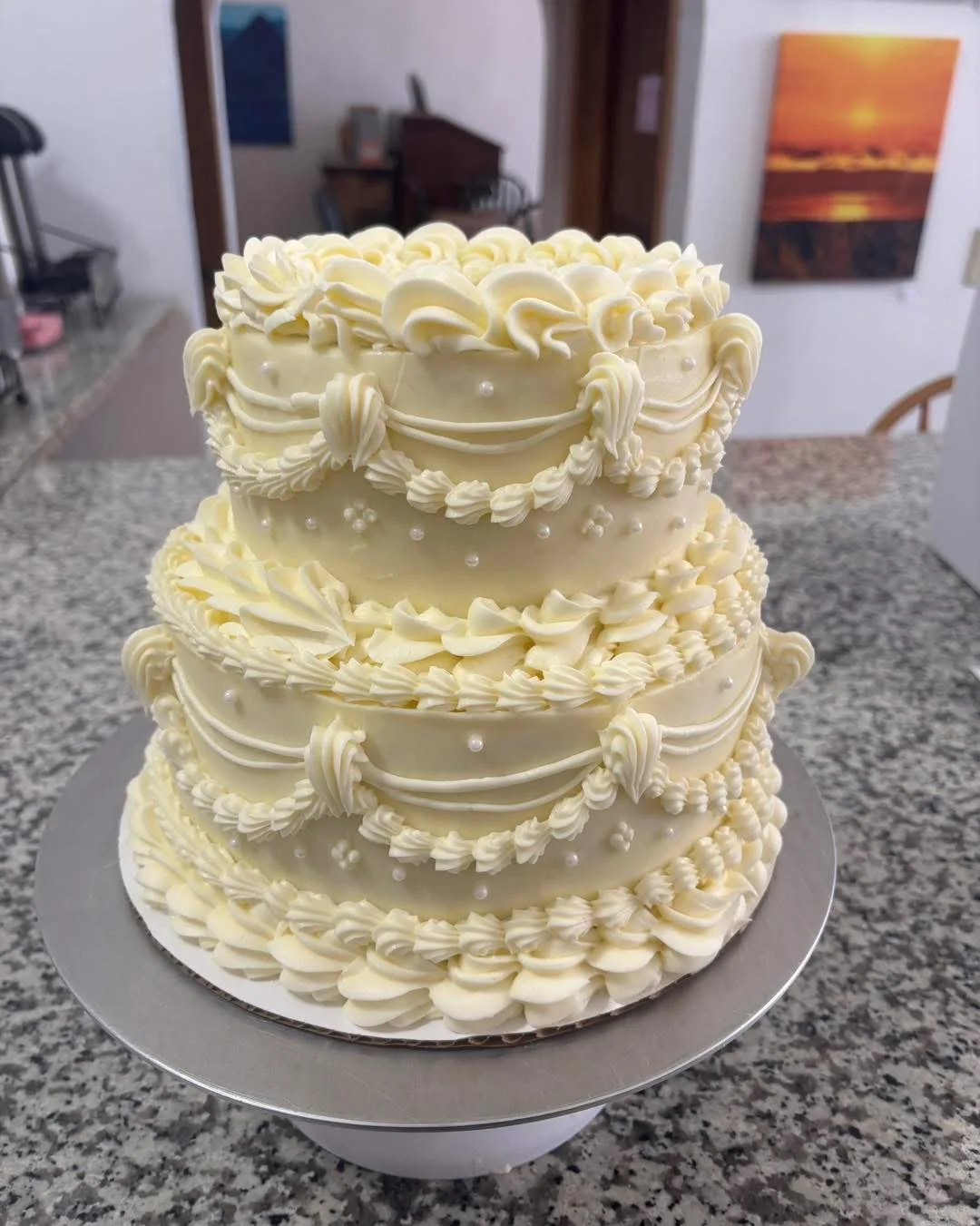 Two-tier ivory buttercream cake with vintage piped swags, ruffled shell borders, and pearl accents on a silver board.