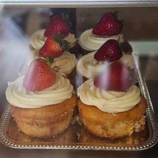 Golden cupcakes with swirls of cream frosting, each topped with a fresh strawberry, arranged on a silver tray.