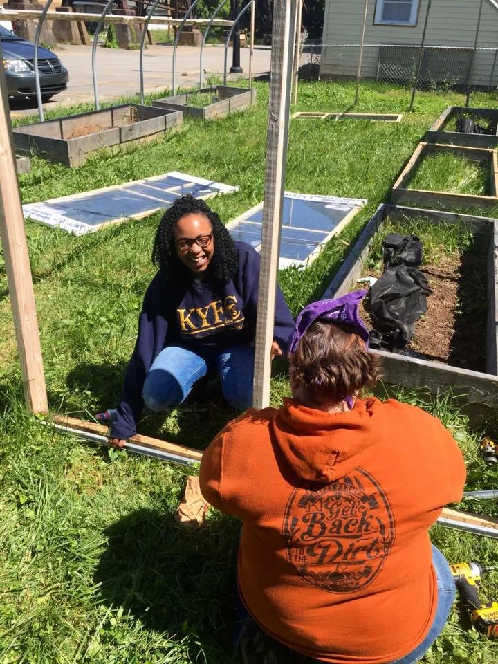 A woman is smiling outside working on constructing a garden bed.