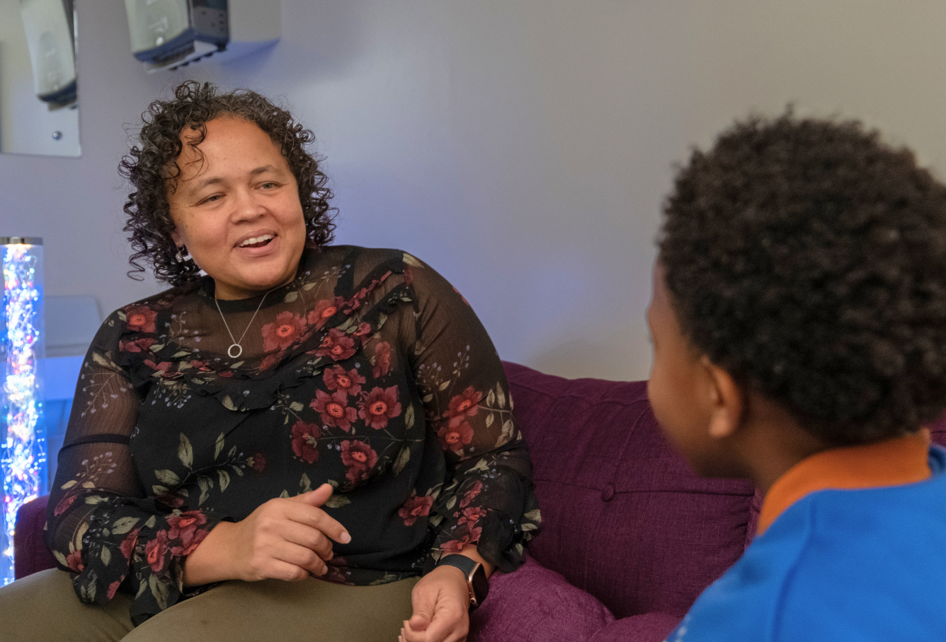 An adult counselor is sitting on a couch smiling at a young child.