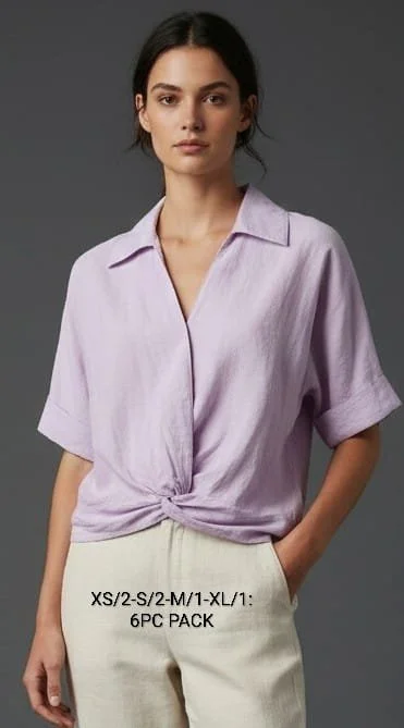 A young woman with shoulder-length wavy brown hair, wearing a light gray button-up shirt with rolled-up sleeves and dark blue jeans, smiling against a plain gray background.