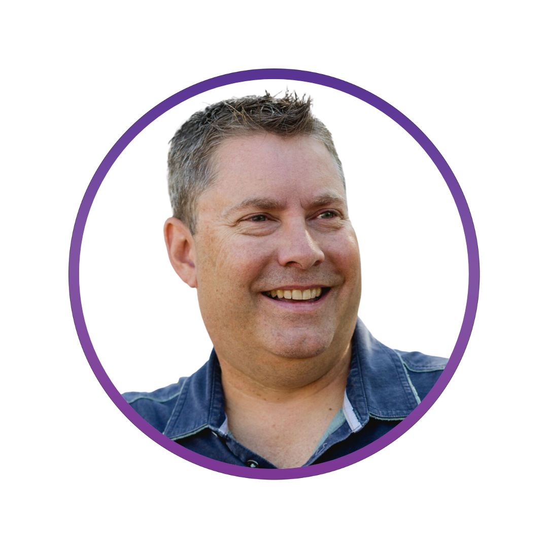 Close-up of a smiling man with short gray hair, wearing a denim shirt, against a white background.