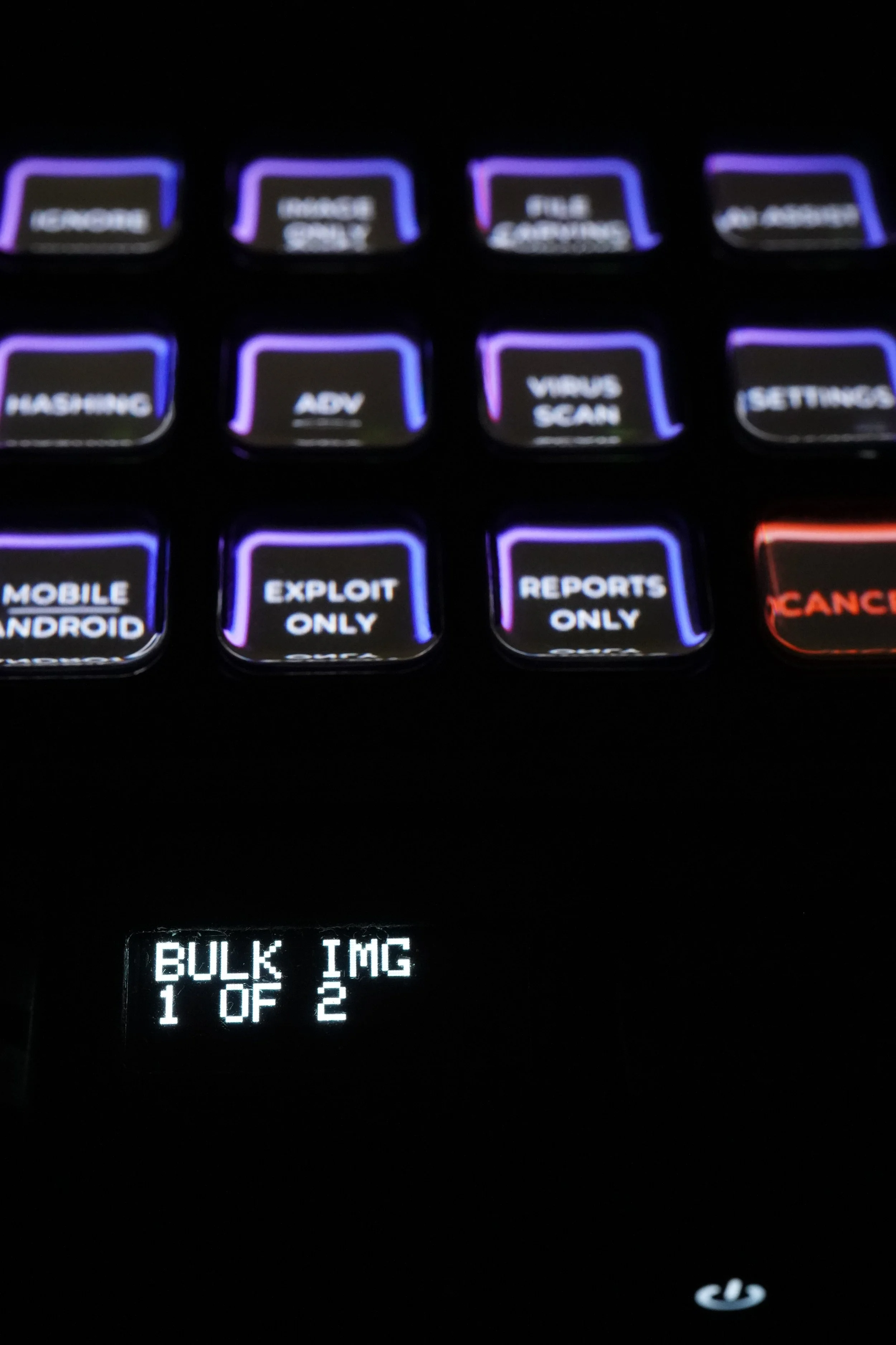 Close-up photo of a computer keyboard with illuminated keys, displaying options such as 'Exploit Only,' 'Reports Only,' and a small screen with 'Bulk Img 1 of 2' text.