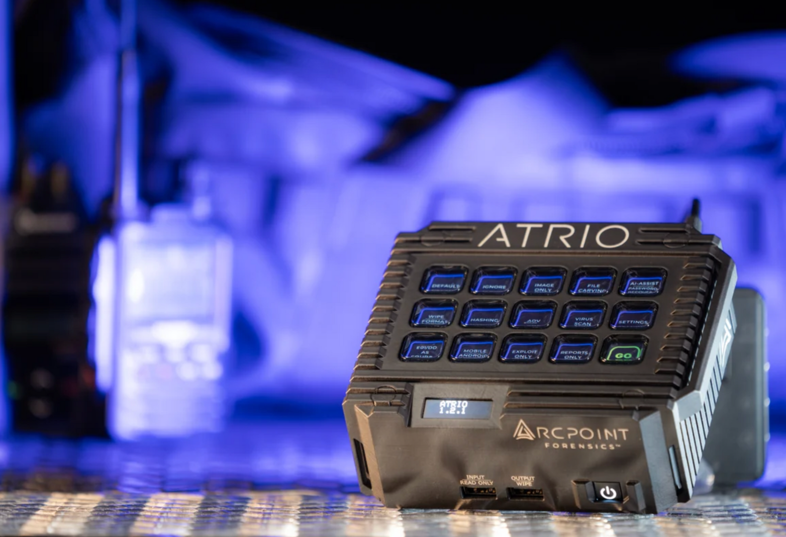 Close-up of a black forensic evidence scanner labeled 'ATRIO' and 'ARCPOINT FORENSICS' on a metallic surface with a blurred background of blue lighting.