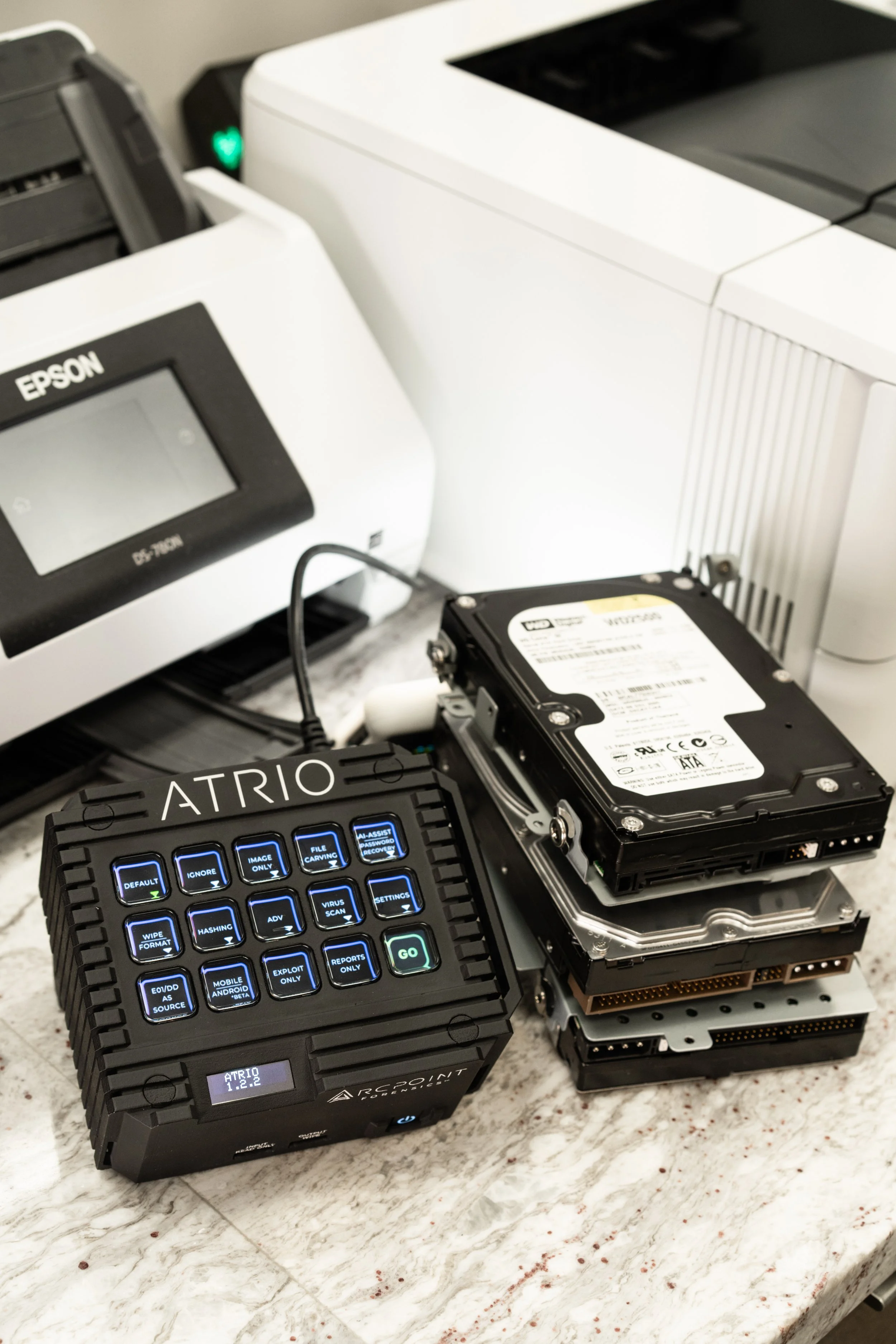 Multiple stacked hard drives connected to a computer diagnostic device on a white marble surface.