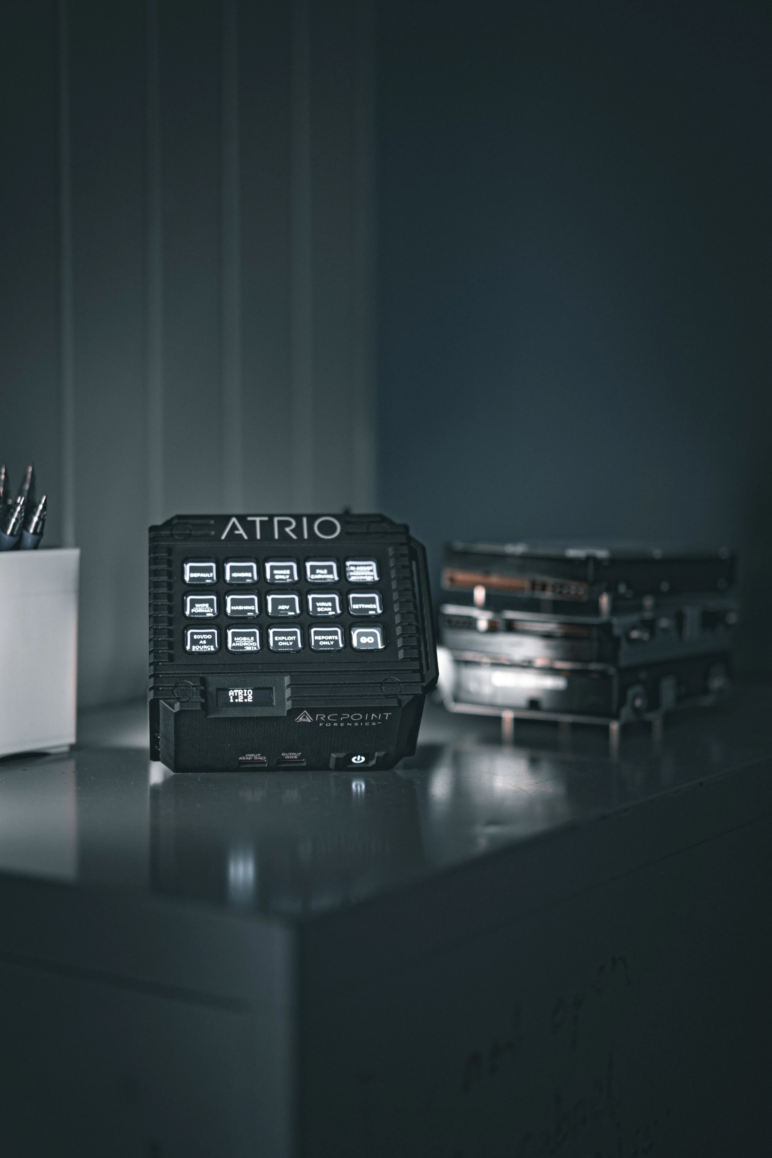 A digital forensics tool called ATRIO on a desk with a stack of external hard drives nearby.