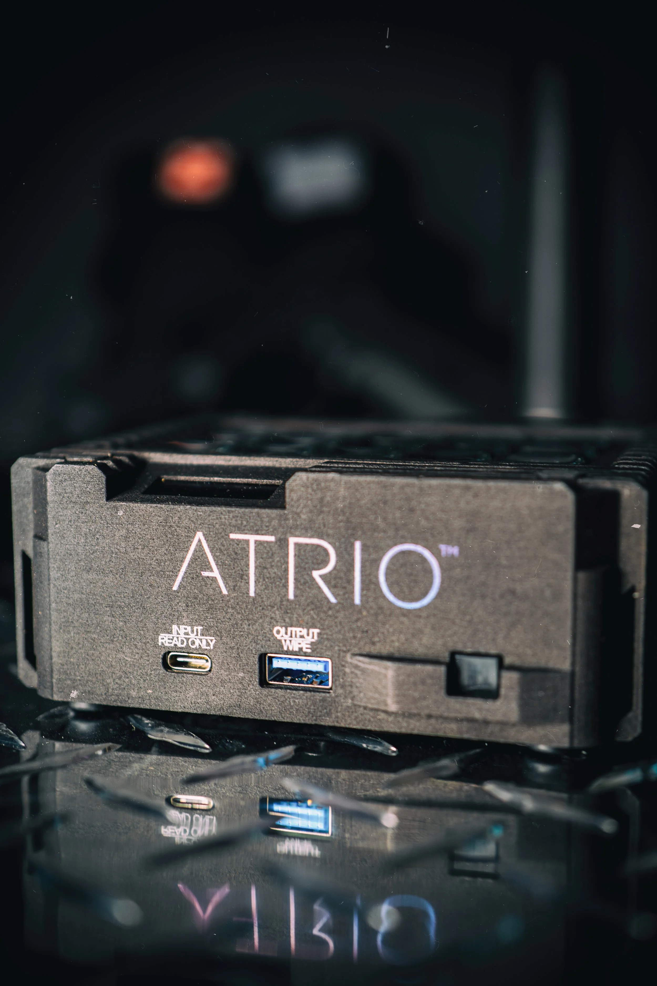 Close-up of a black electronic device labeled 'ATRIO' with a USB-C port and a USB type-A port, reflected on a shiny surface.