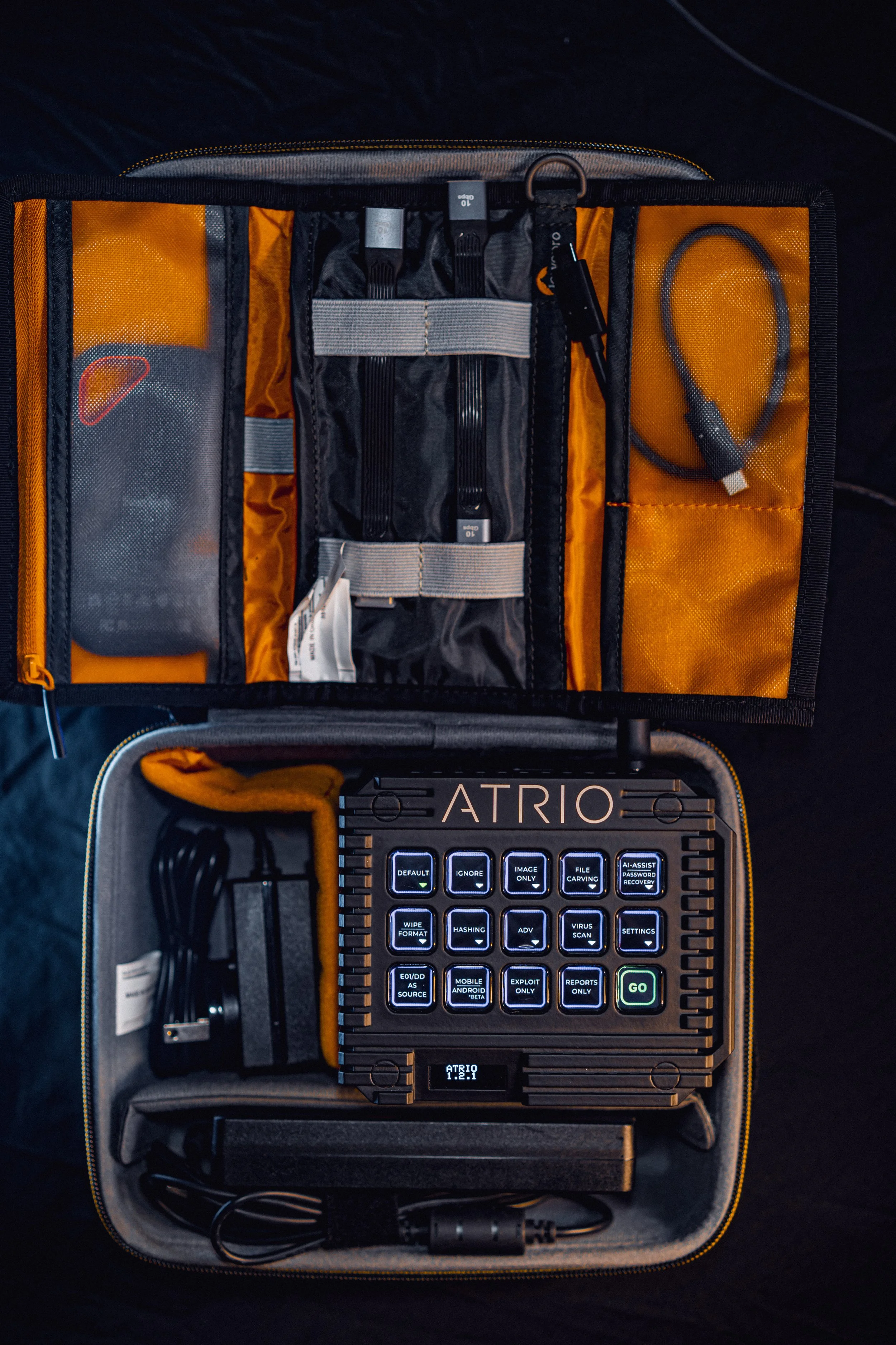 An electronic device with keys in a case, along with cables and accessories, organized in a structured bag with compartments.
