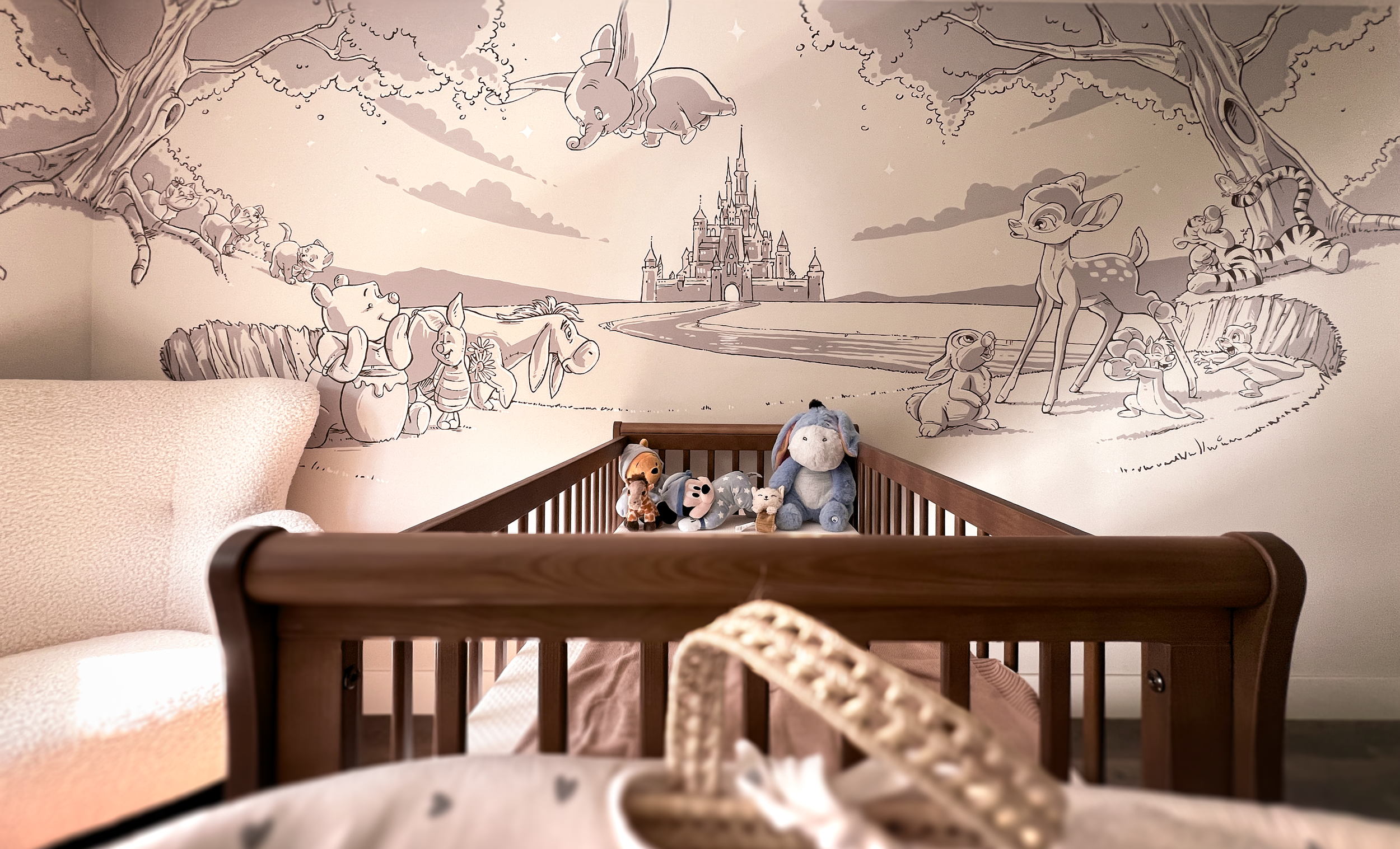 Een babykamer met een muurtekening van een sprookjesachtig kasteel en dieren zoals een olifant, een giraf, een beer, een hertjes en muisjes. Er liggen knuffeldieren in het ledikant.