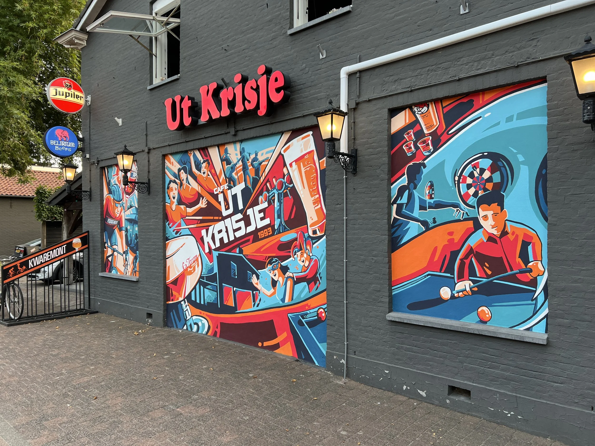 De gevel van een gebouw met kleurrijke street art-muurschilderingen en neonborden van café 'ut Krisje'.