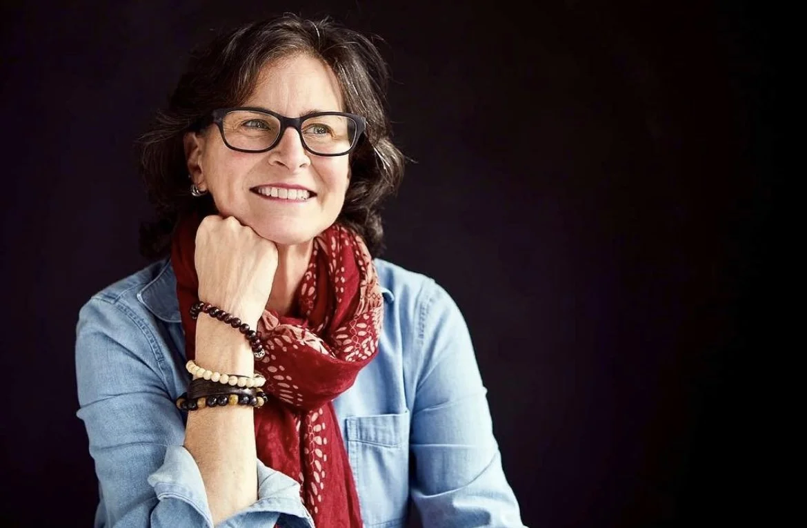 Smiling woman with glasses, wearing a denim shirt and red scarf