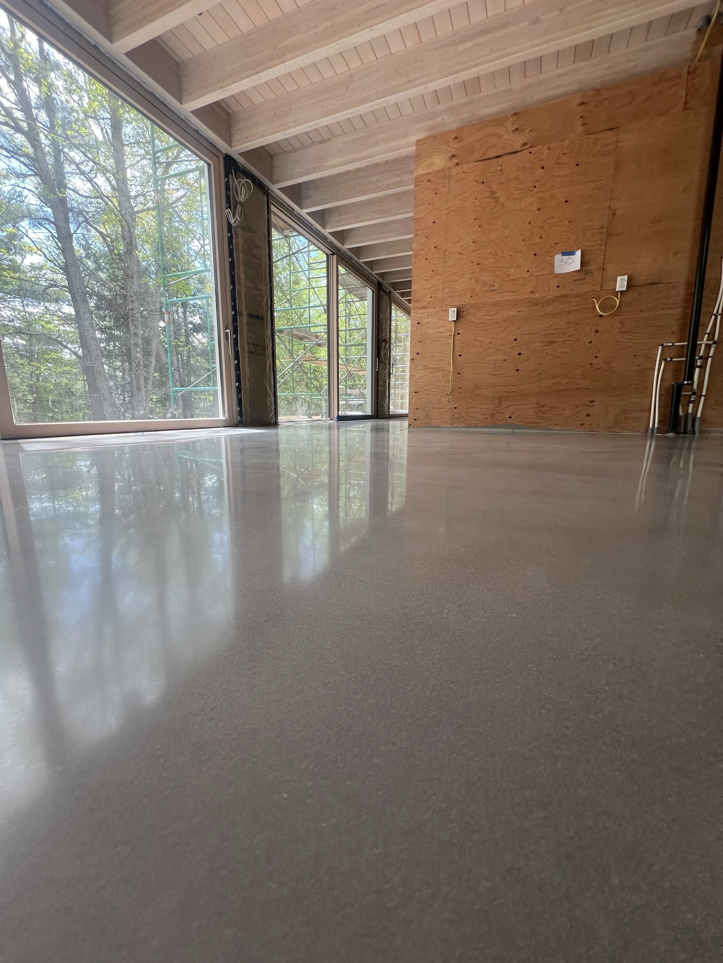 Empty room under construction with large windows, a wood-paneled wall, electrical outlets, and a shiny polished floor.