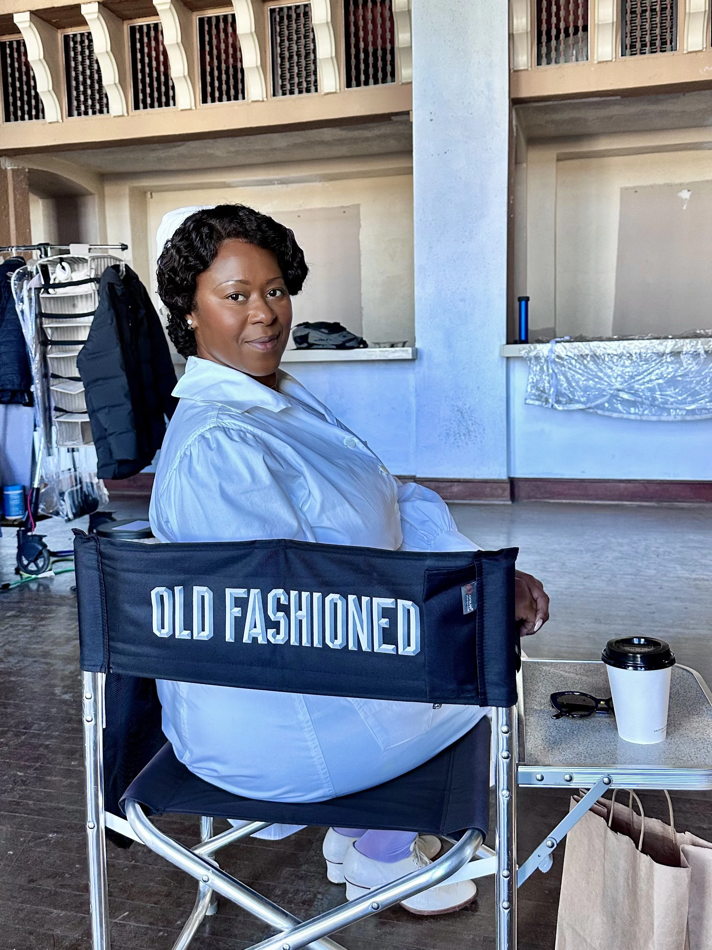 An actor, Treisa Gary is sitting in a cast chair on the set of Spider Noir.