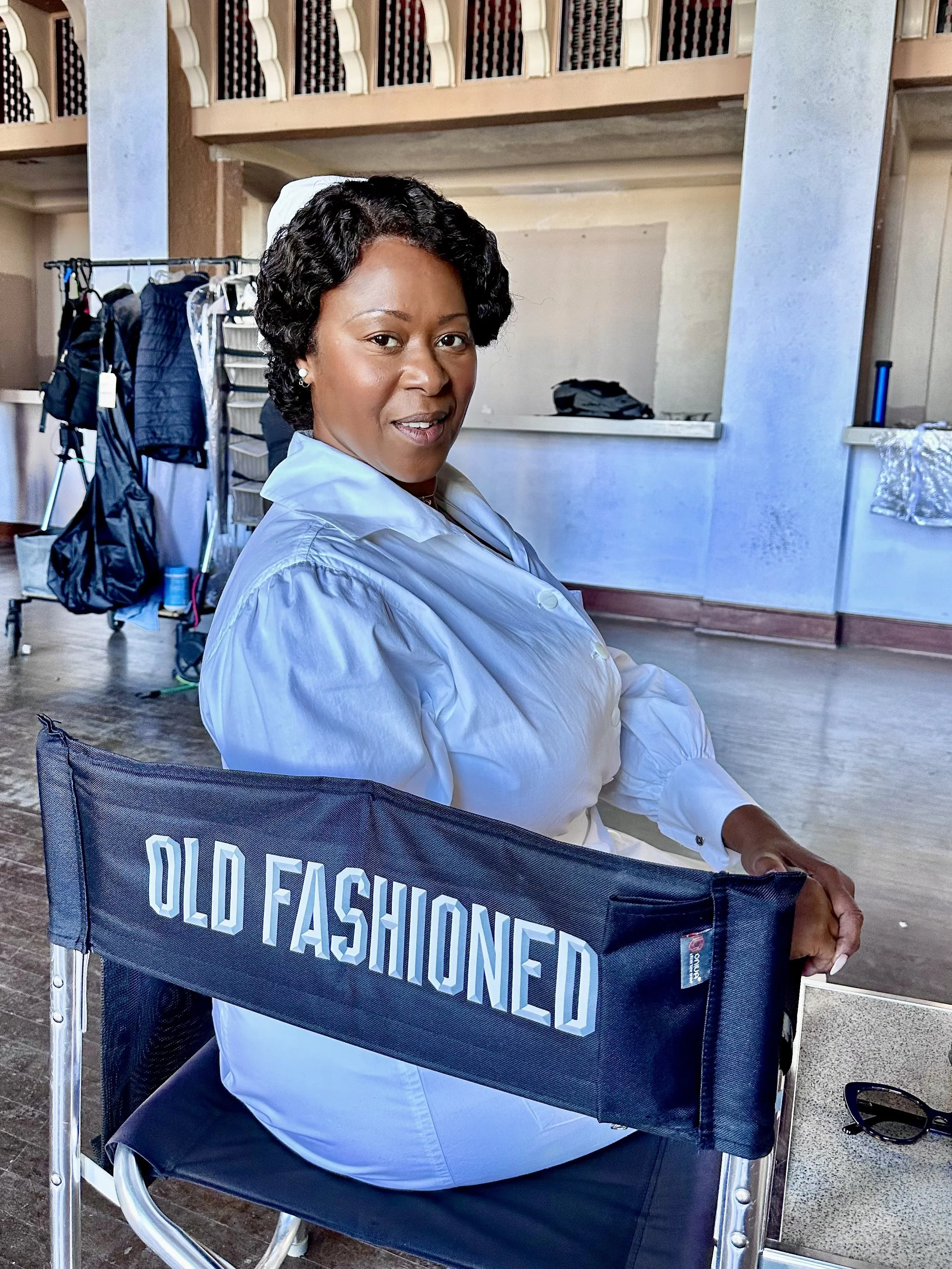 An actor, Treisa Gary is sitting in a cast chair on the set of Spider Noir.