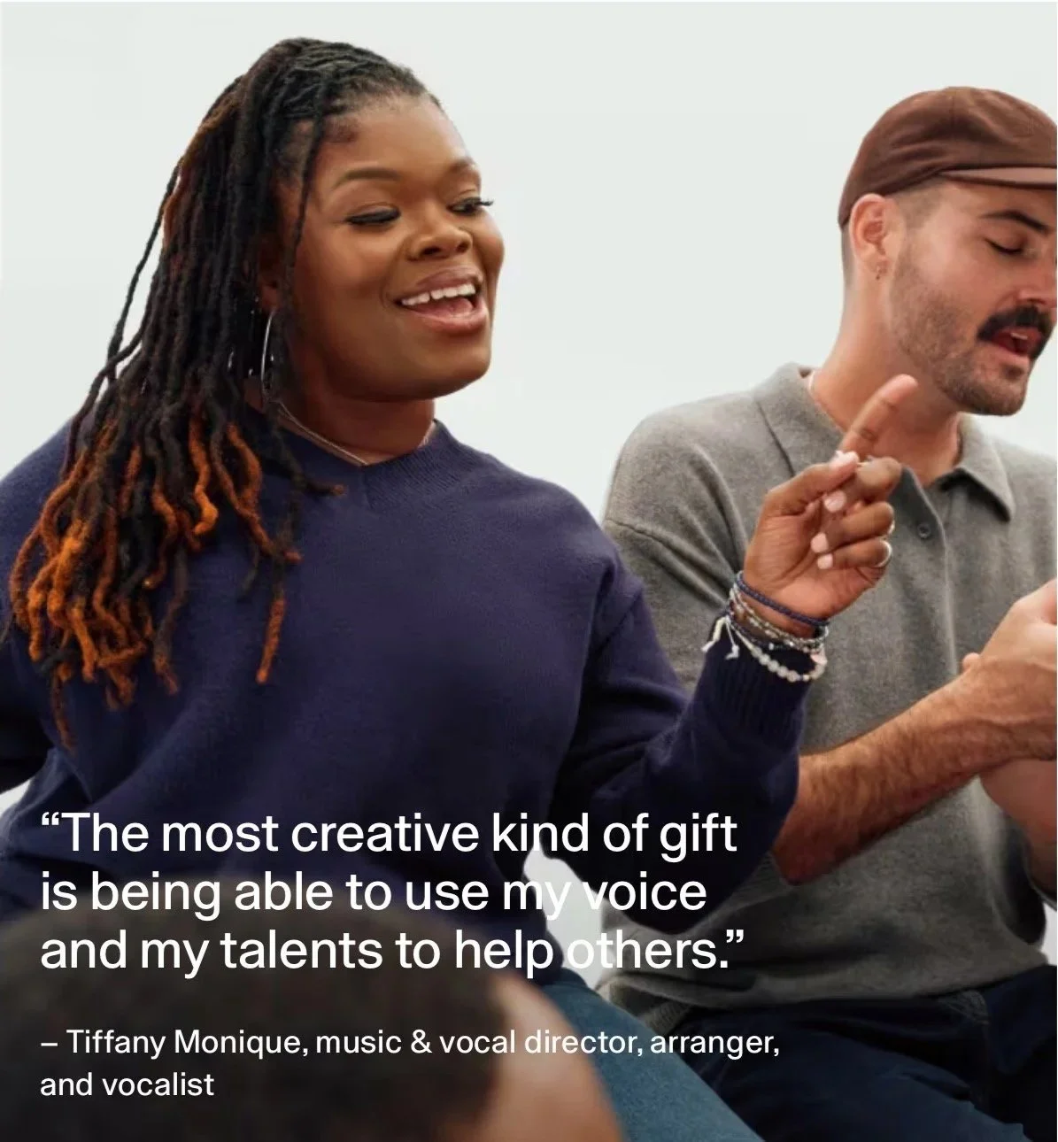 A woman with long dreadlocks smiling and talking, wearing a navy sweater. Next to her, a man with brown hair and a beard, looking at a phone, wearing a gray shirt. The image features a quote from Tiffany Monique about using her voice and talents to help others.