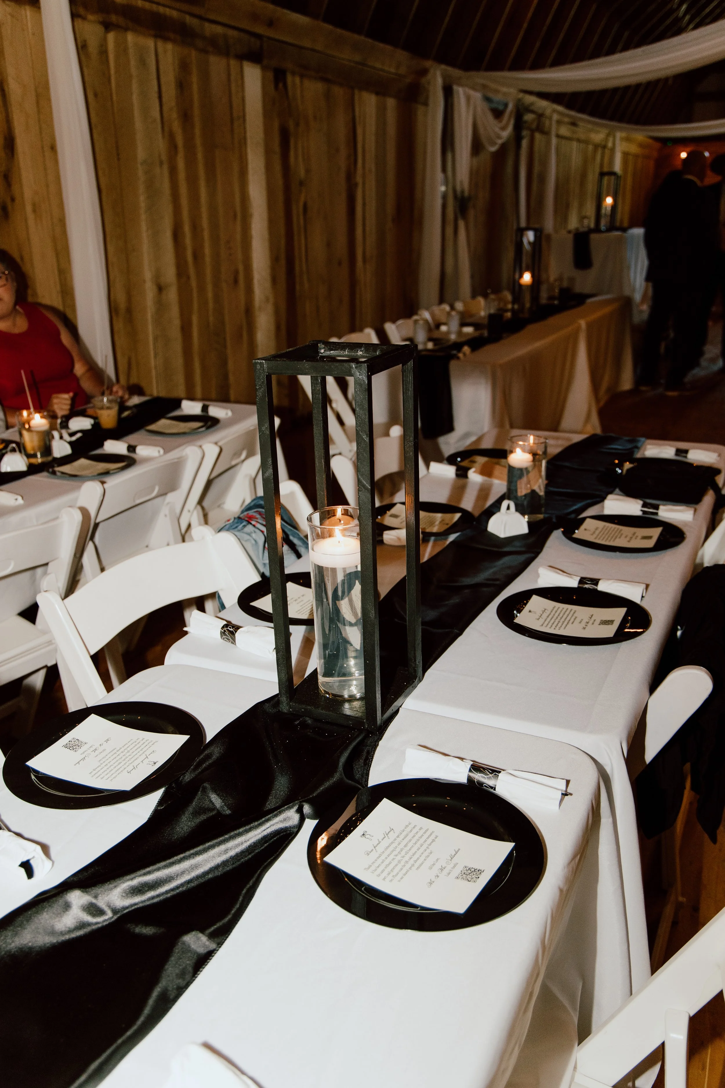 Wedding reception table decorated with black and white theme, featuring candles in glass holders and a black table runner.