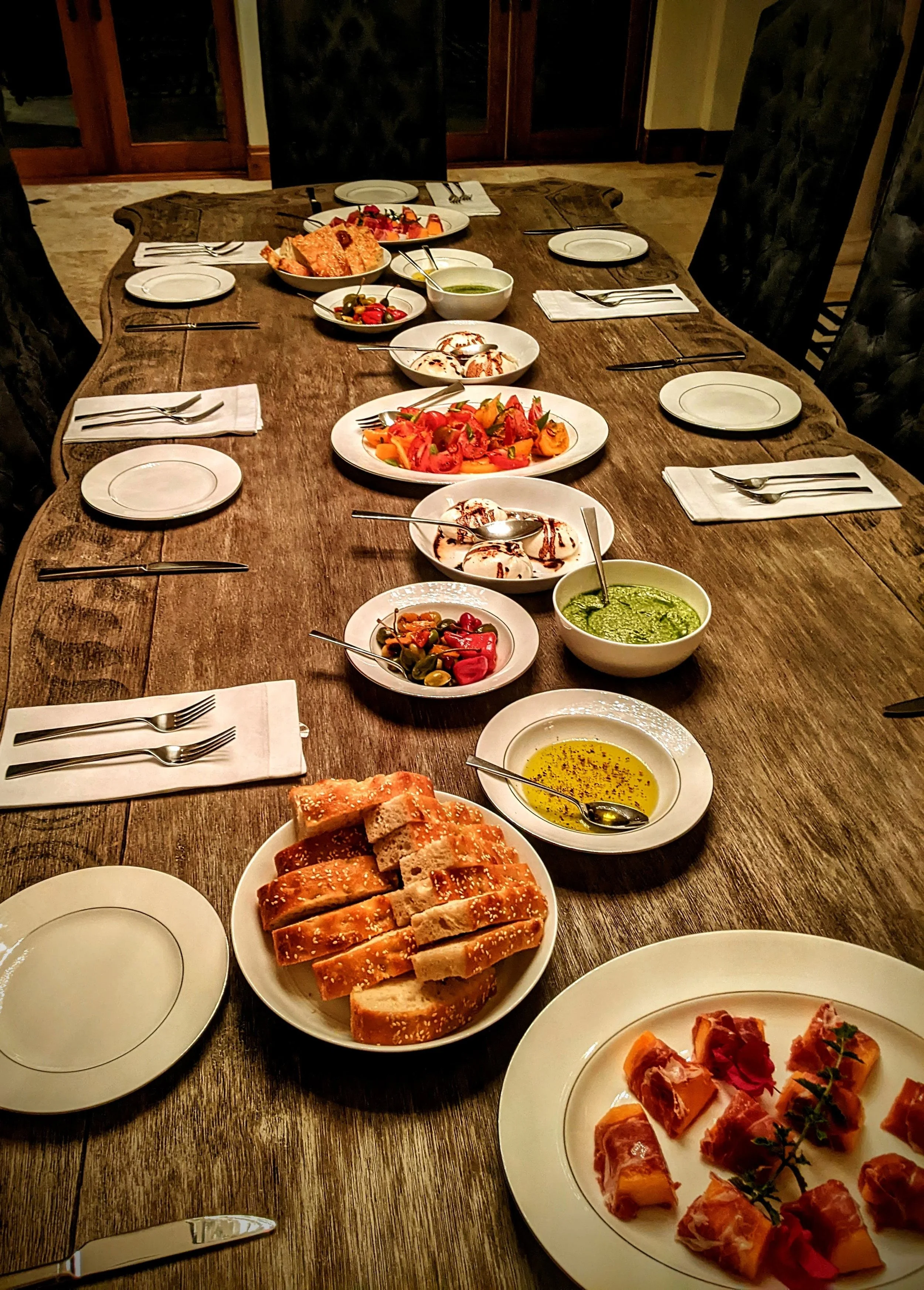 A dining table set with various dishes including breads, salads, dips, and appetizers, with plates, cutlery, and napkins arranged around the table.