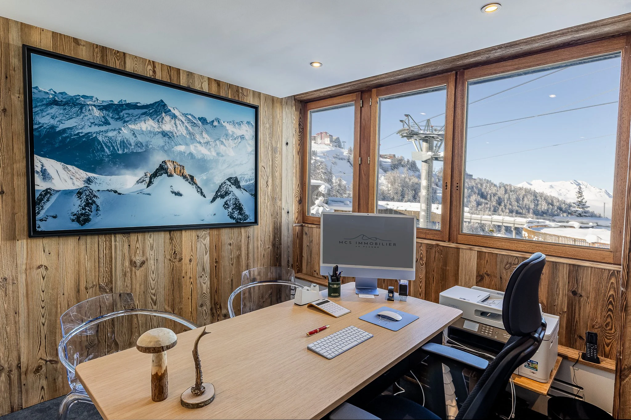 Bureau avec bureau, fauteuil, écran d'ordinateur, vue sur la montagne enneigée par fenêtres en bois.