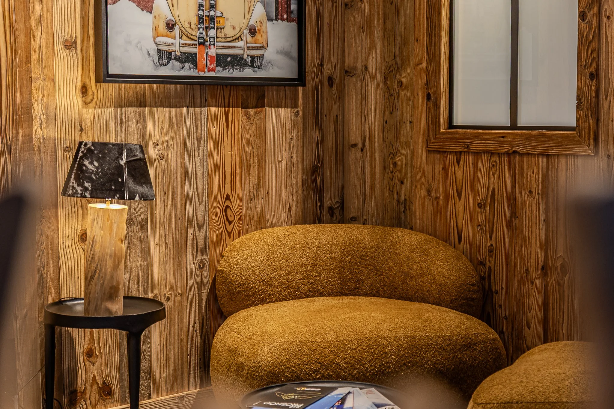 Coin salon avec un canapé marron et une lampe de table en bois, mur en bois, tableau d'une voiture vintage, fenêtre avec cadre en bois.