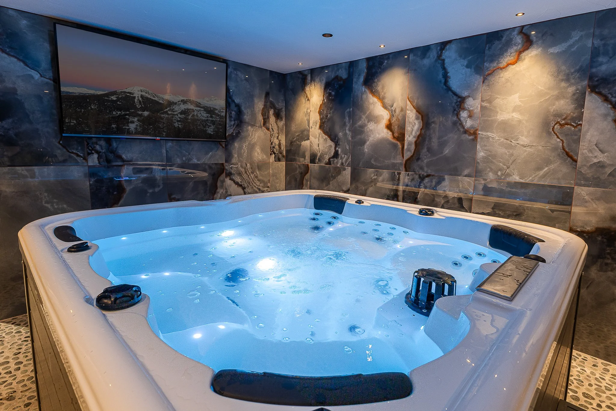 Spa chaud avec jets dans une pièce équipée d'un mur en marbre sombre et d'une grande télévision montée au mur.
