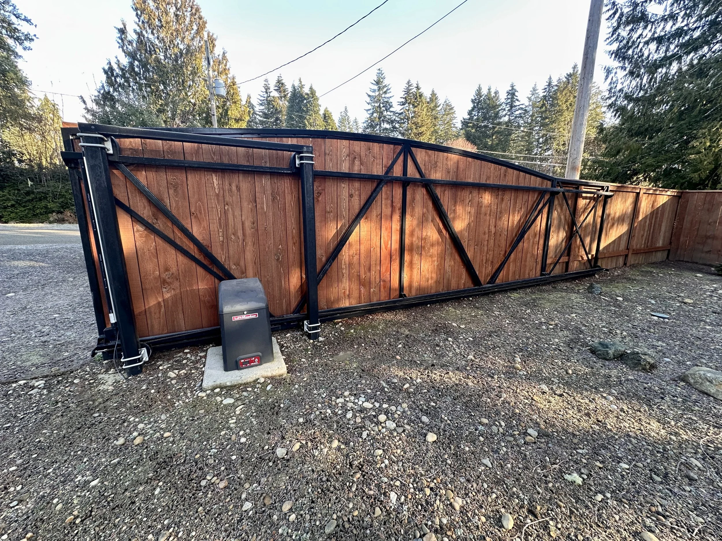 A large, wooden sliding automatic gate with black steel or aluminum support accent frames.