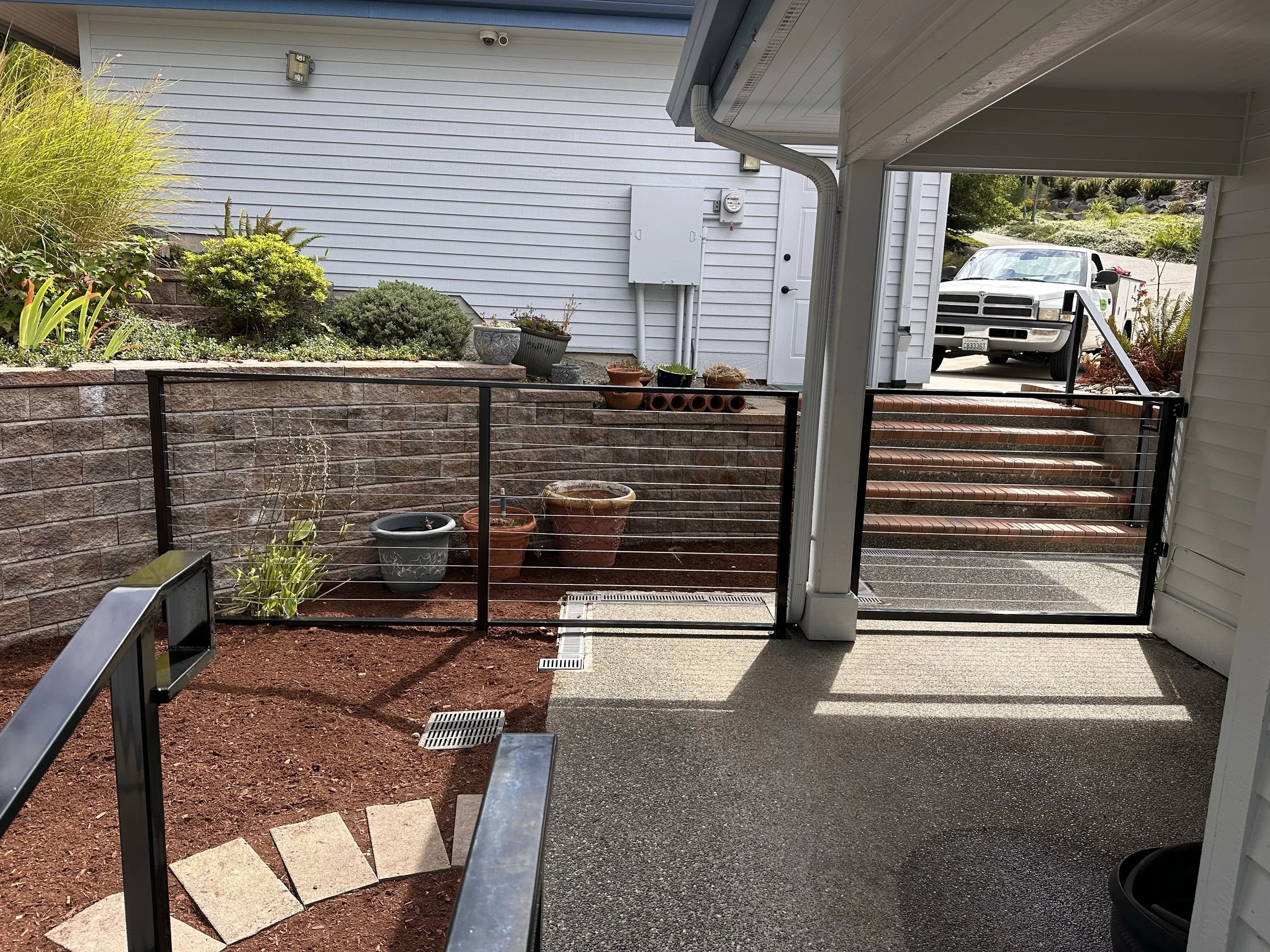 A hardscaped backyard patio with a custom metal fence and hardscape features like study stairway hand rails.