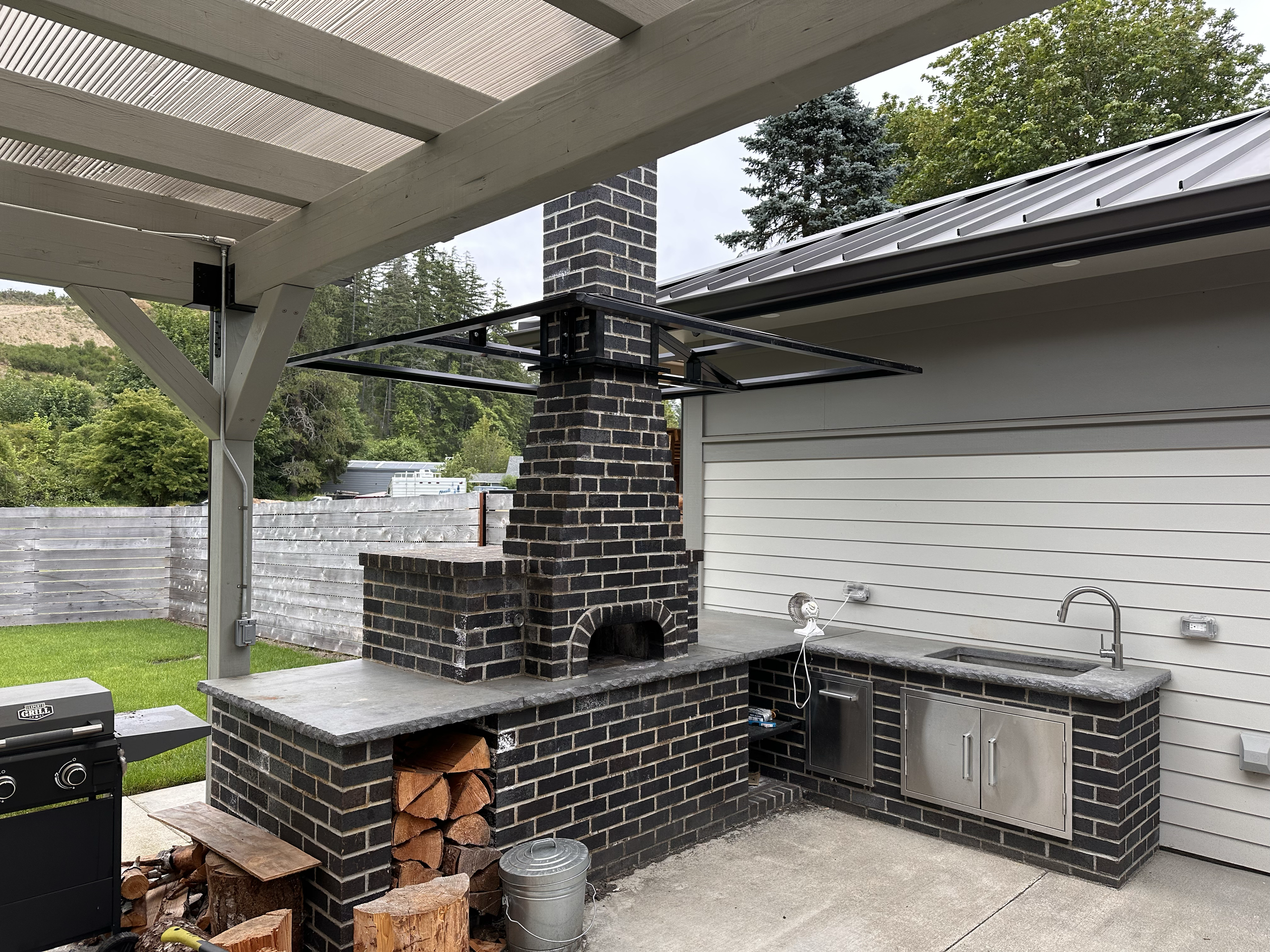 A rustic hand-built brick outdoor garden kitchen, featuring a full sink and oven.