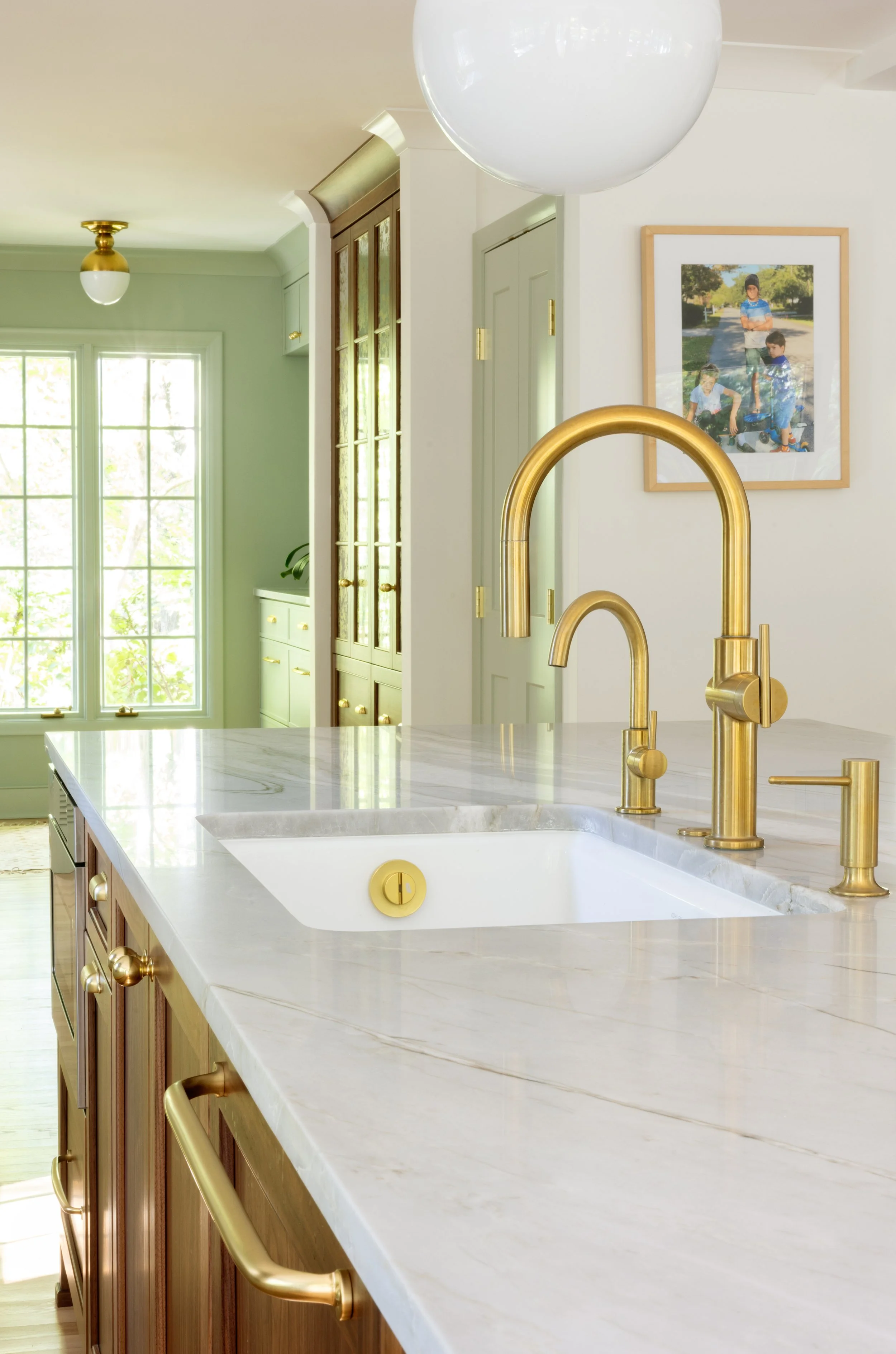 Bright kitchen with marble countertop, gold fixtures, and a framed family photo on the wall.