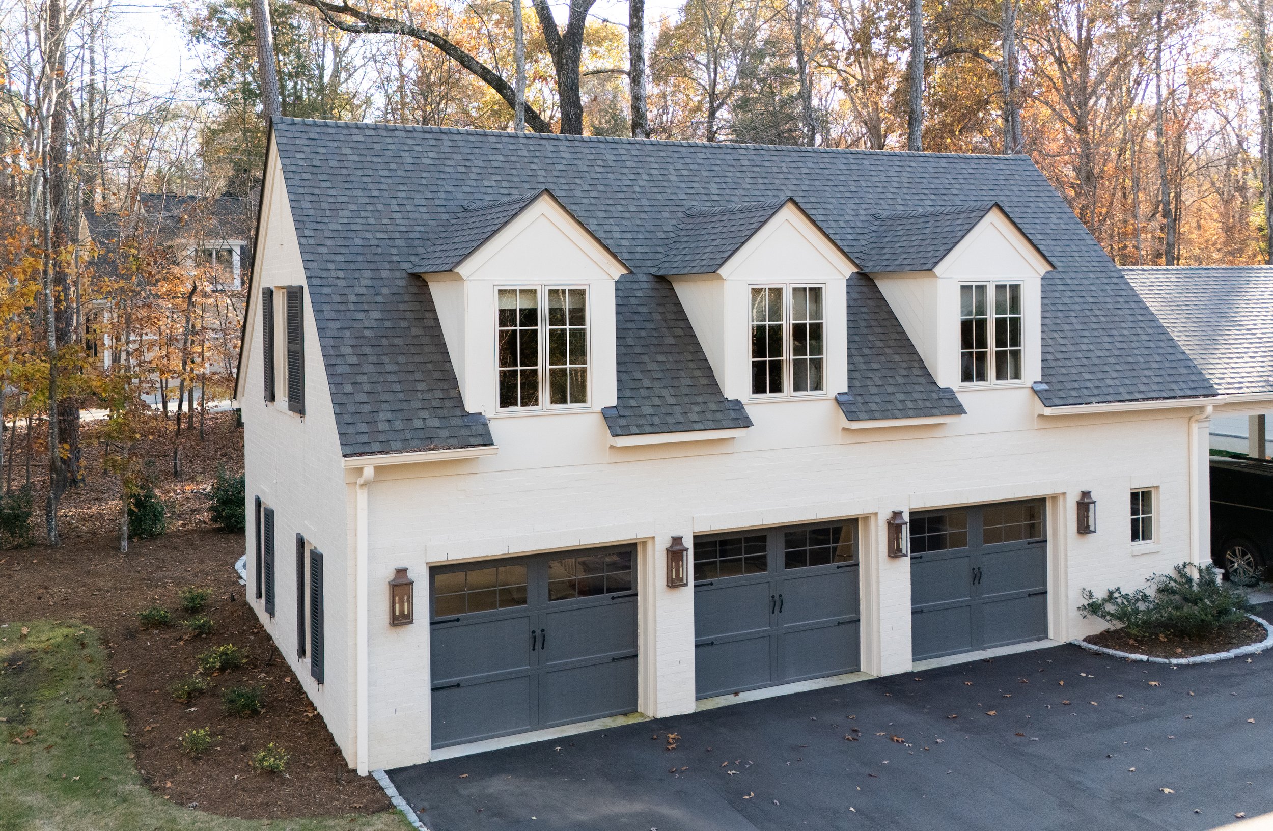 A two-story white house with black shutters and a dark gray shingled roof, featuring three dormer windows.
