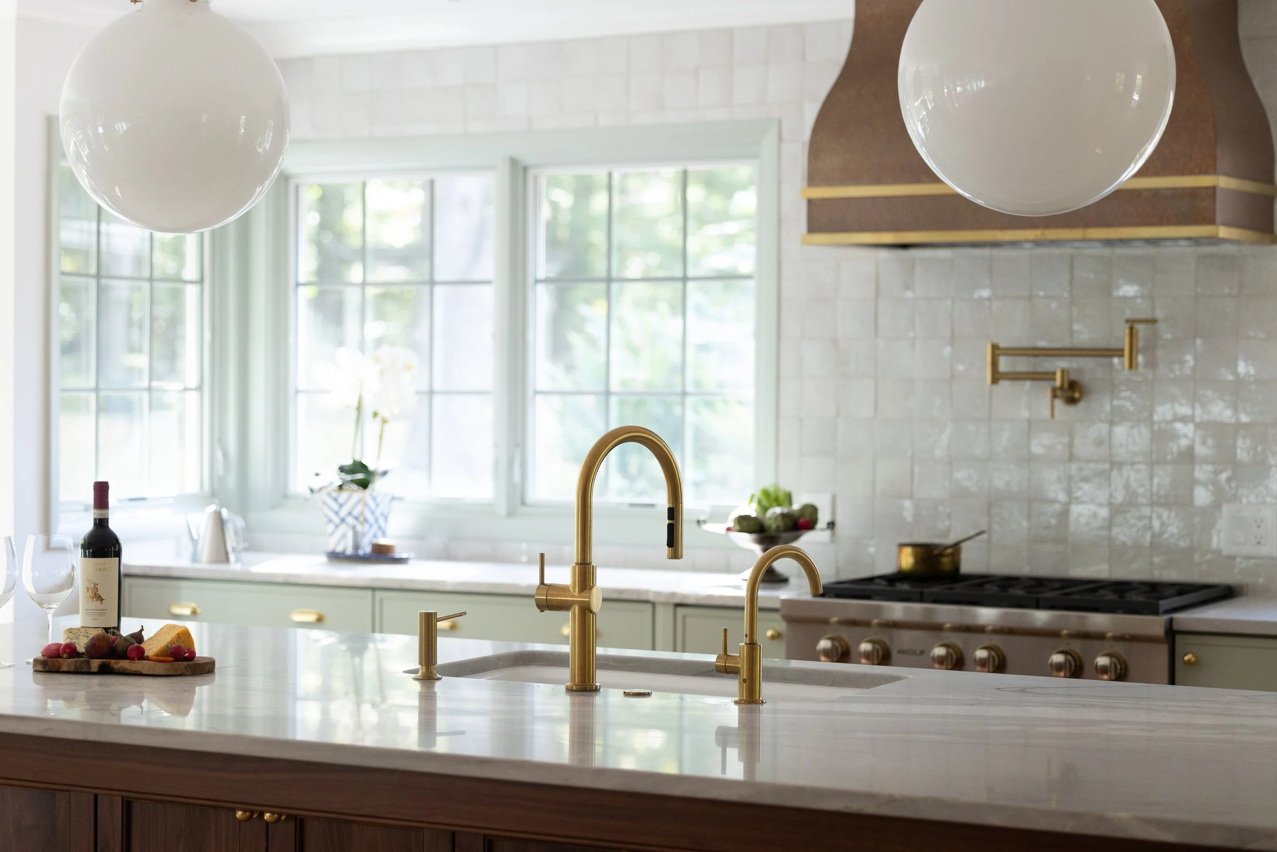Kitchen interior of a luxury custom home by Will Johnson Building Company in the Triangle NC featuring a large island, brass fixtures, range hood, and bright natural light