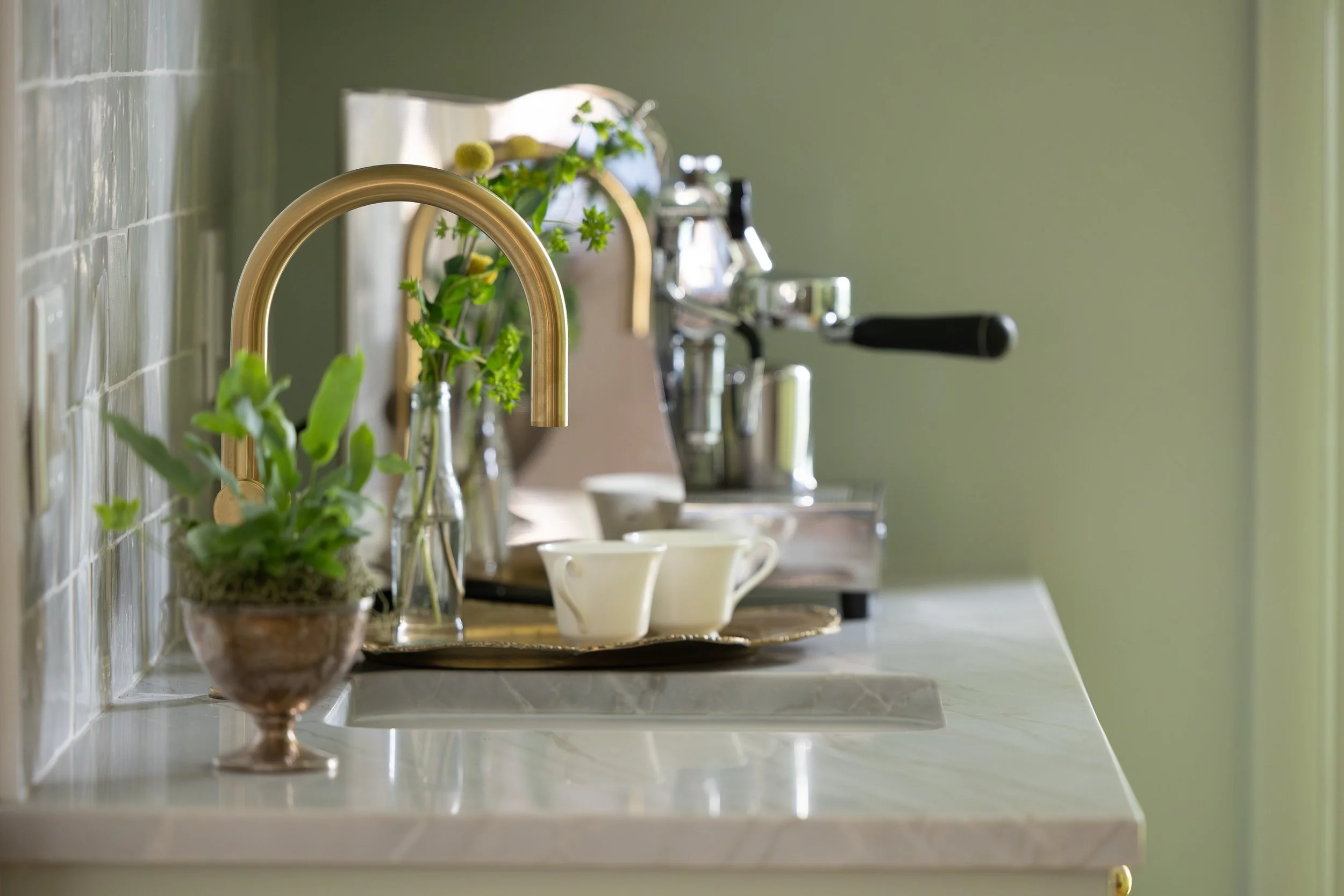 Luxury coffee and beverage station with brass fixtures, marble countertop, espresso setup, and layered natural light in a Triangle custom kitchen