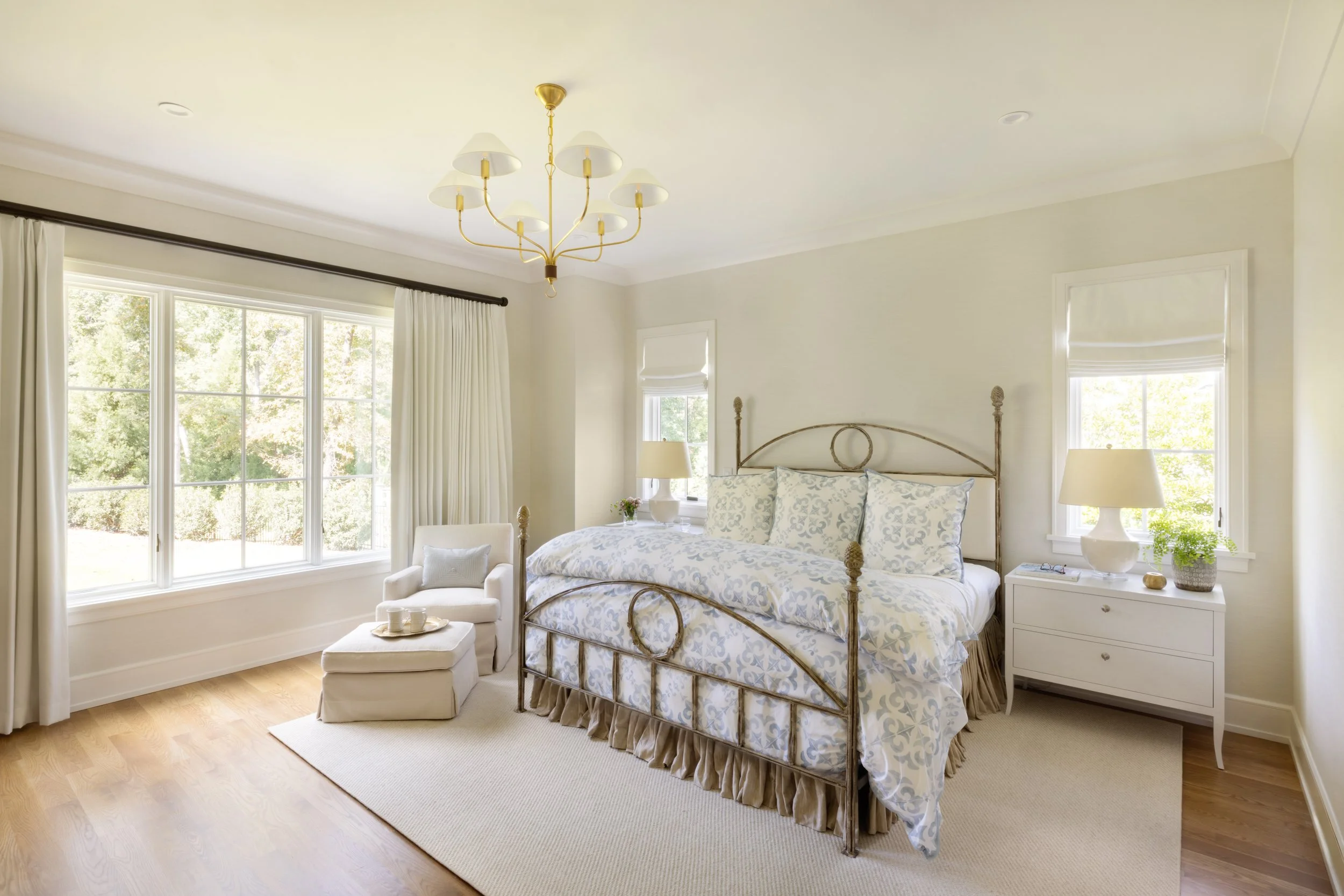 Primary suite bedroom with classic metal bed, soft neutral finishes, and natural light designed for quiet luxury living