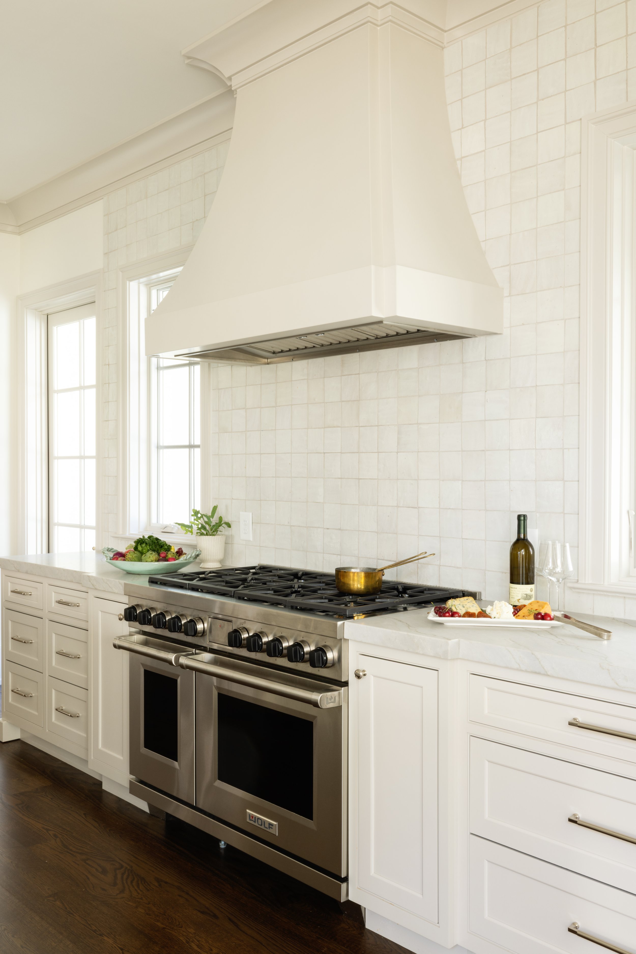 A kitchen with white cabinets, a stove with double ovens, a white range hood, and a backsplash with light-colored tiles.