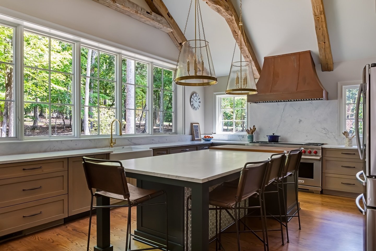 The heart of our client&rsquo;s home: a kitchen adorned with natural materials, rustic wood beams, and a distinctive patinated copper hood. Our team enjoyed working with our clients, who grew up in Ireland, to create a unique vision for this space. T
