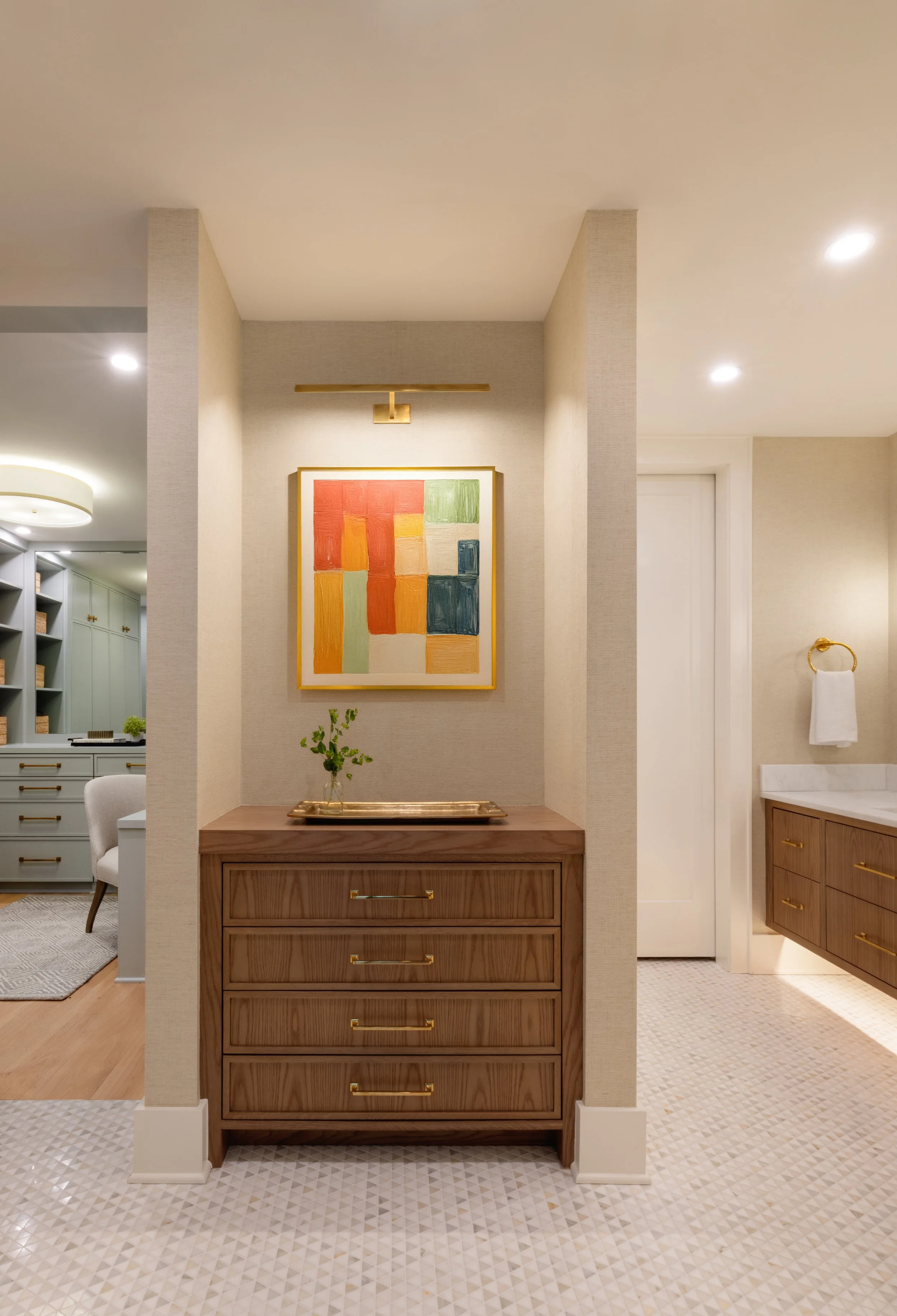 Interior of a modern home with a wooden dresser, framed abstract art, and a vase with green foliage on the dresser, decorated in neutral tones with gold accents.