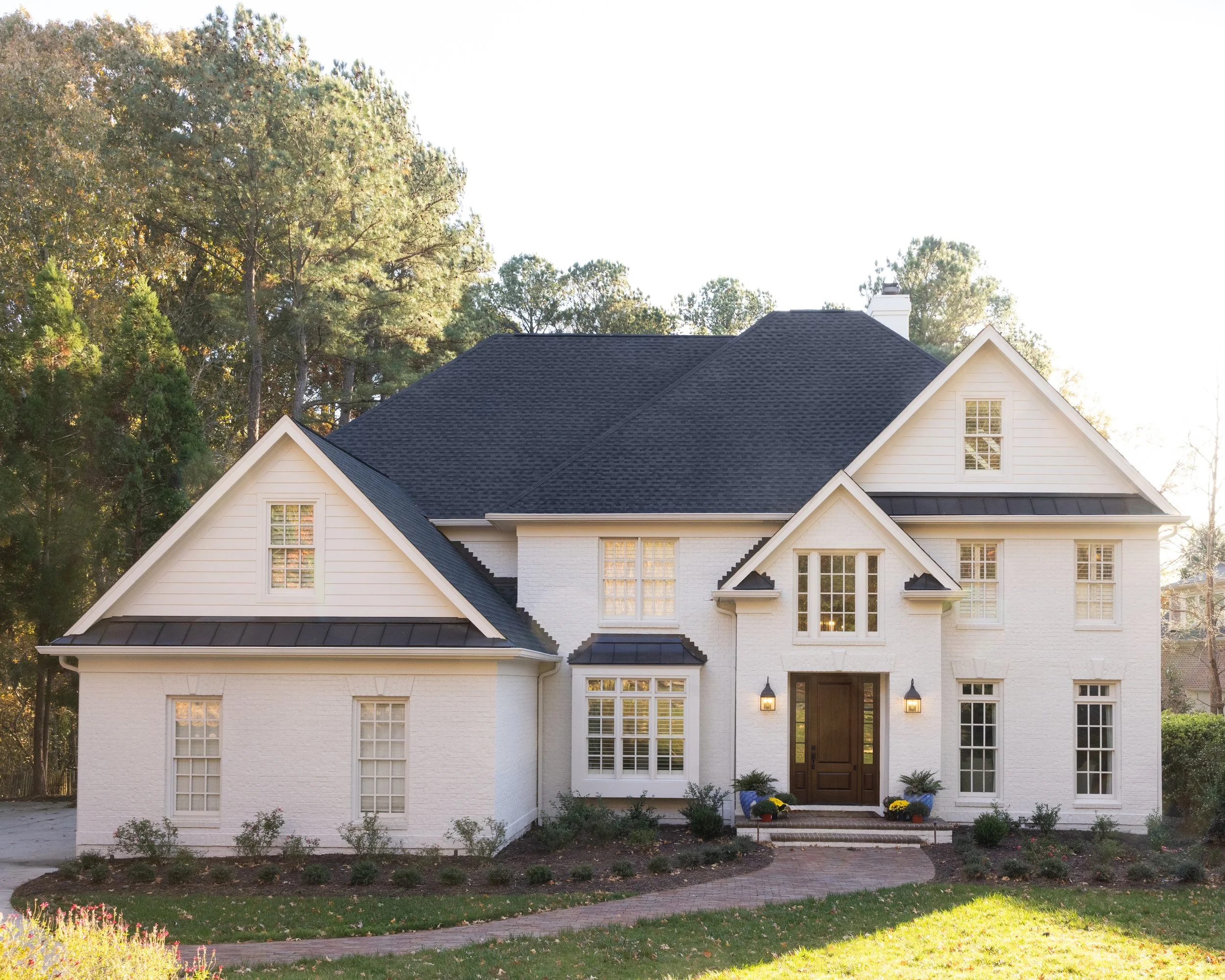 Front exterior of a luxury custom home by Will Johnson Building Company in the Triangle NC featuring light siding, gabled rooflines, black windows, and a landscaped yard with classic residential design