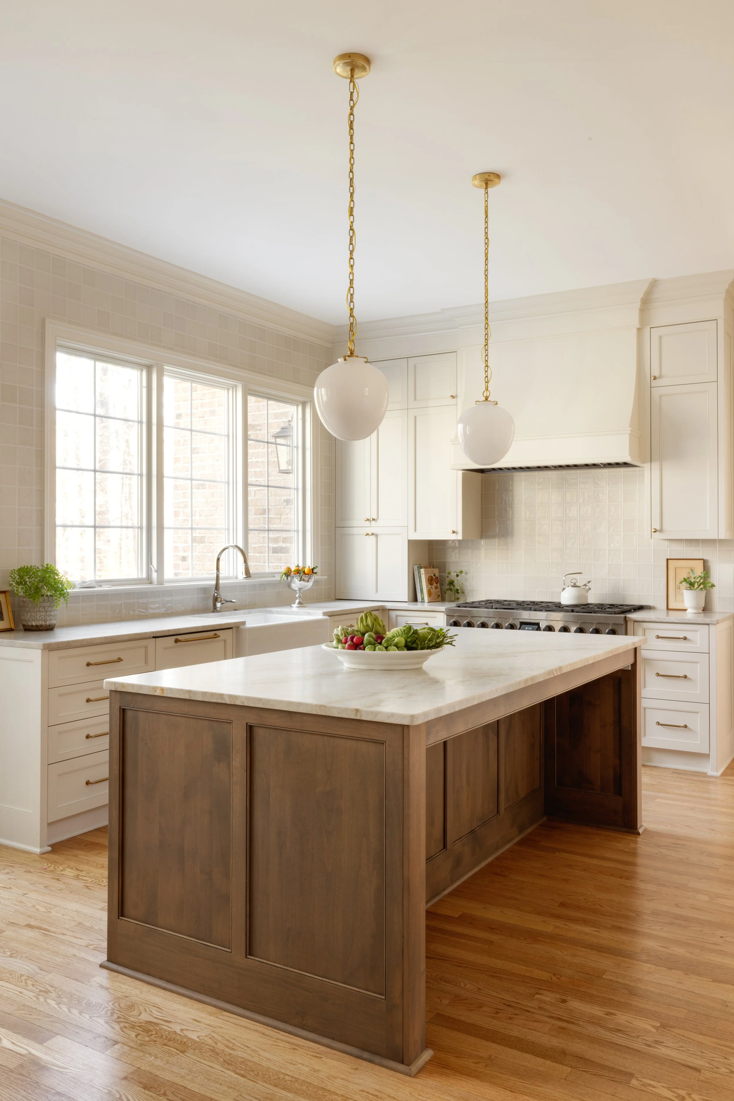 A bright kitchen with white cabinetry, a kitchen island with a wooden base and white countertop, pendant lights, and large windows letting in natural light.