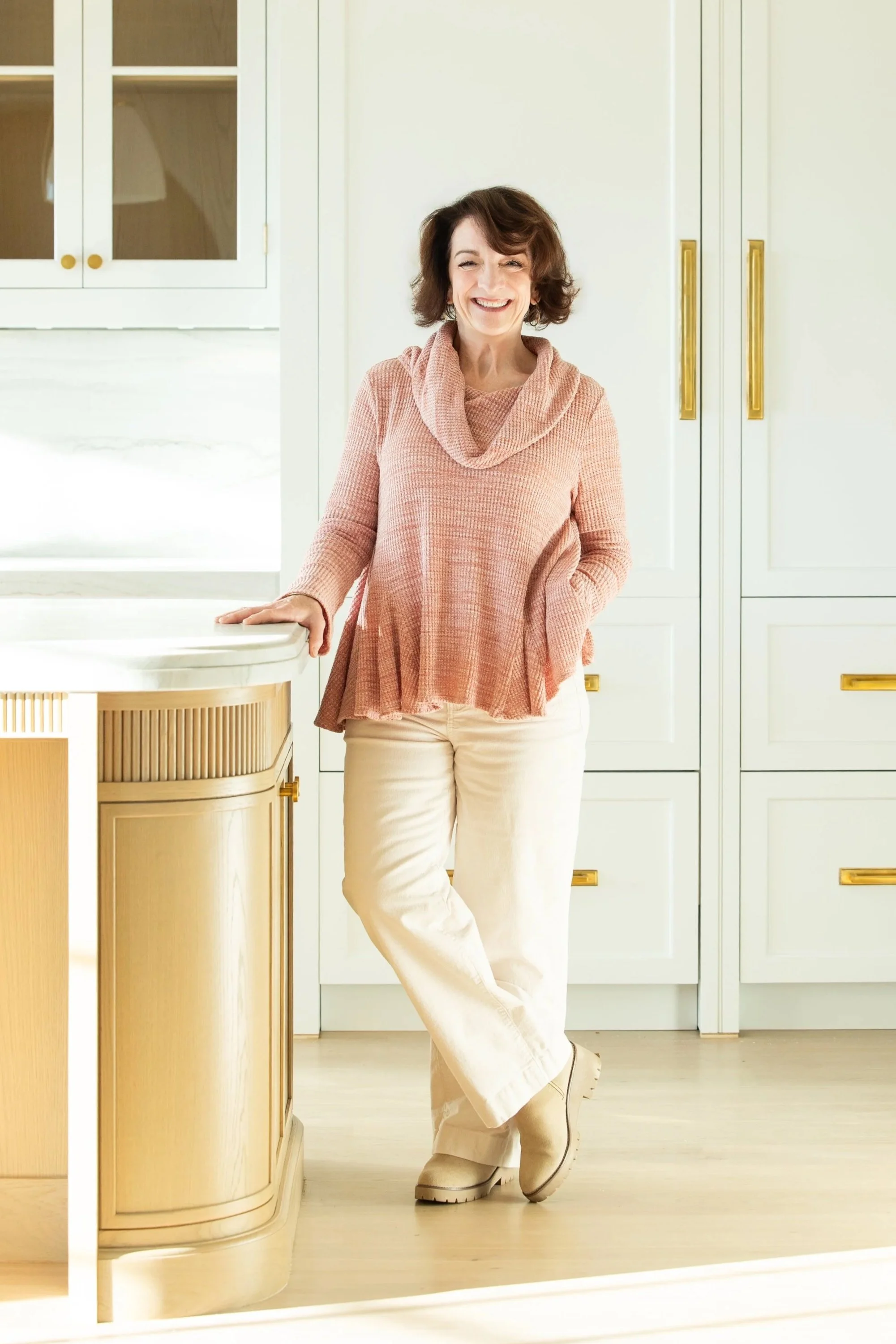 Woman sitting at a desk with a laptop and fabric samples, smiling, in a modern interior design office.