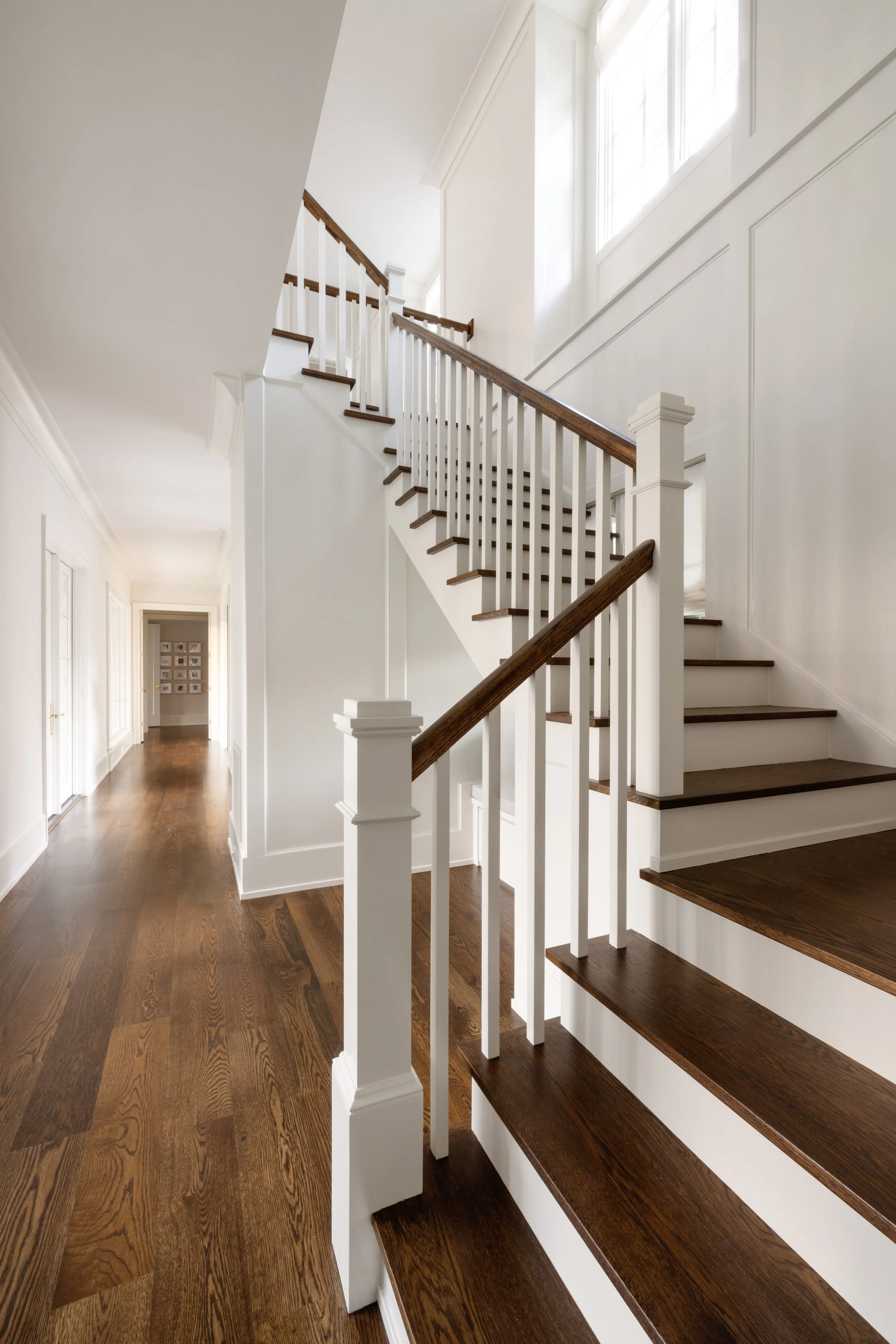 Interior view of a staircase with dark wood steps and white railings, leading to an upper floor in a bright, modern home.