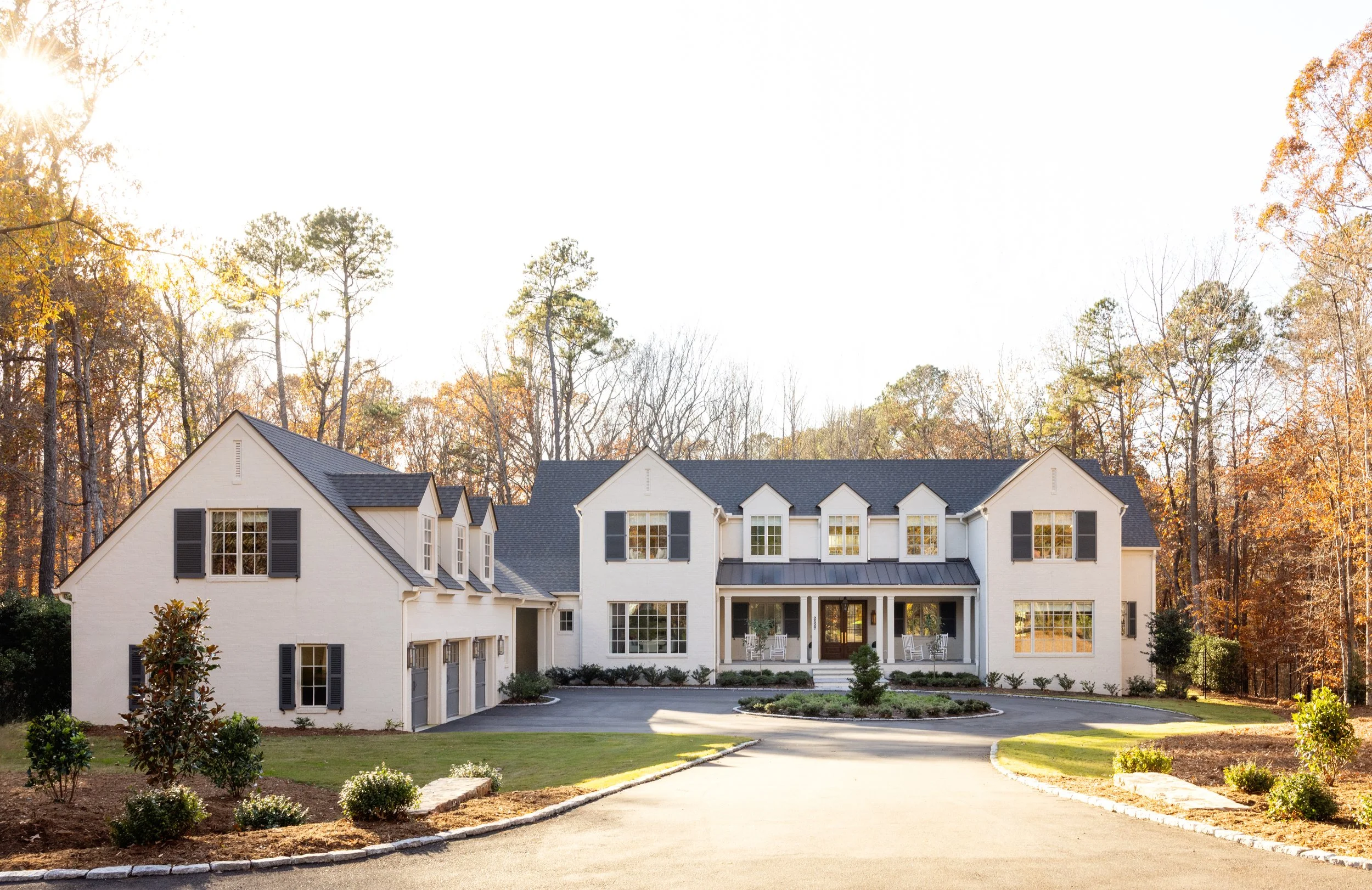 Large modern house with white exterior and black shutters, surrounded by trees and landscaped yard, with a curved driveway leading to the front entrance.