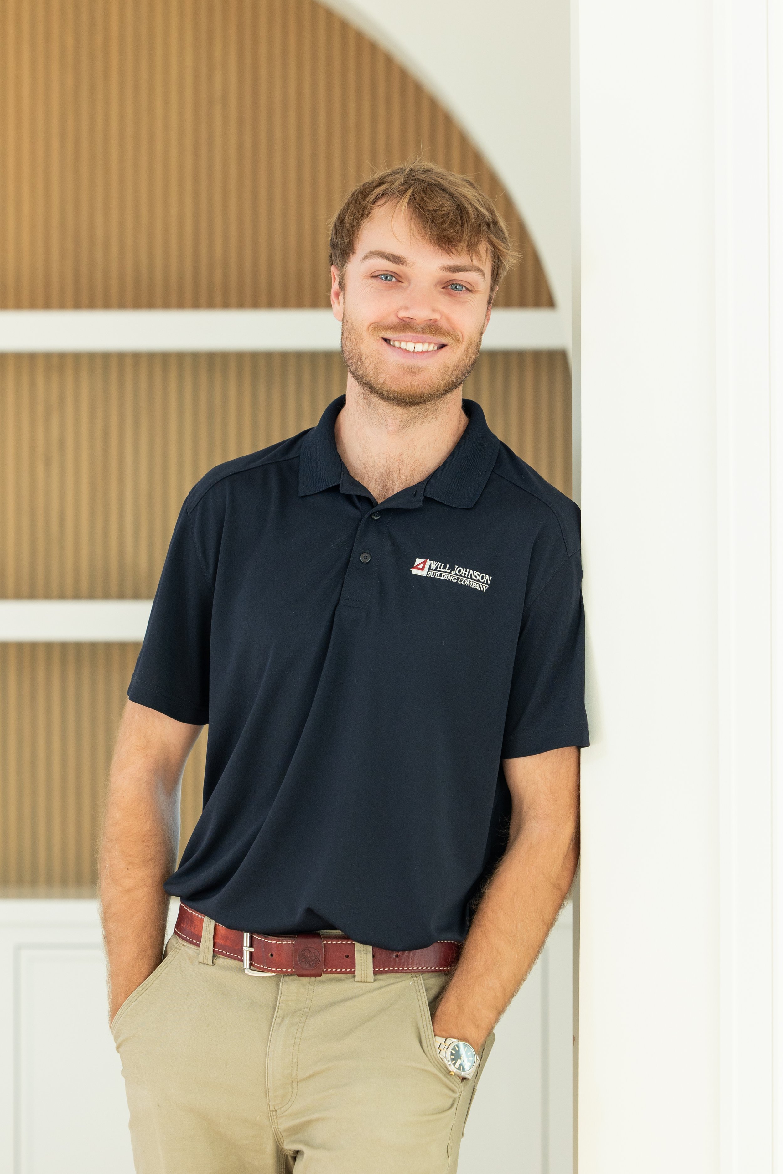 Person sitting at a table with architectural plans and a laptop, smiling at the camera.