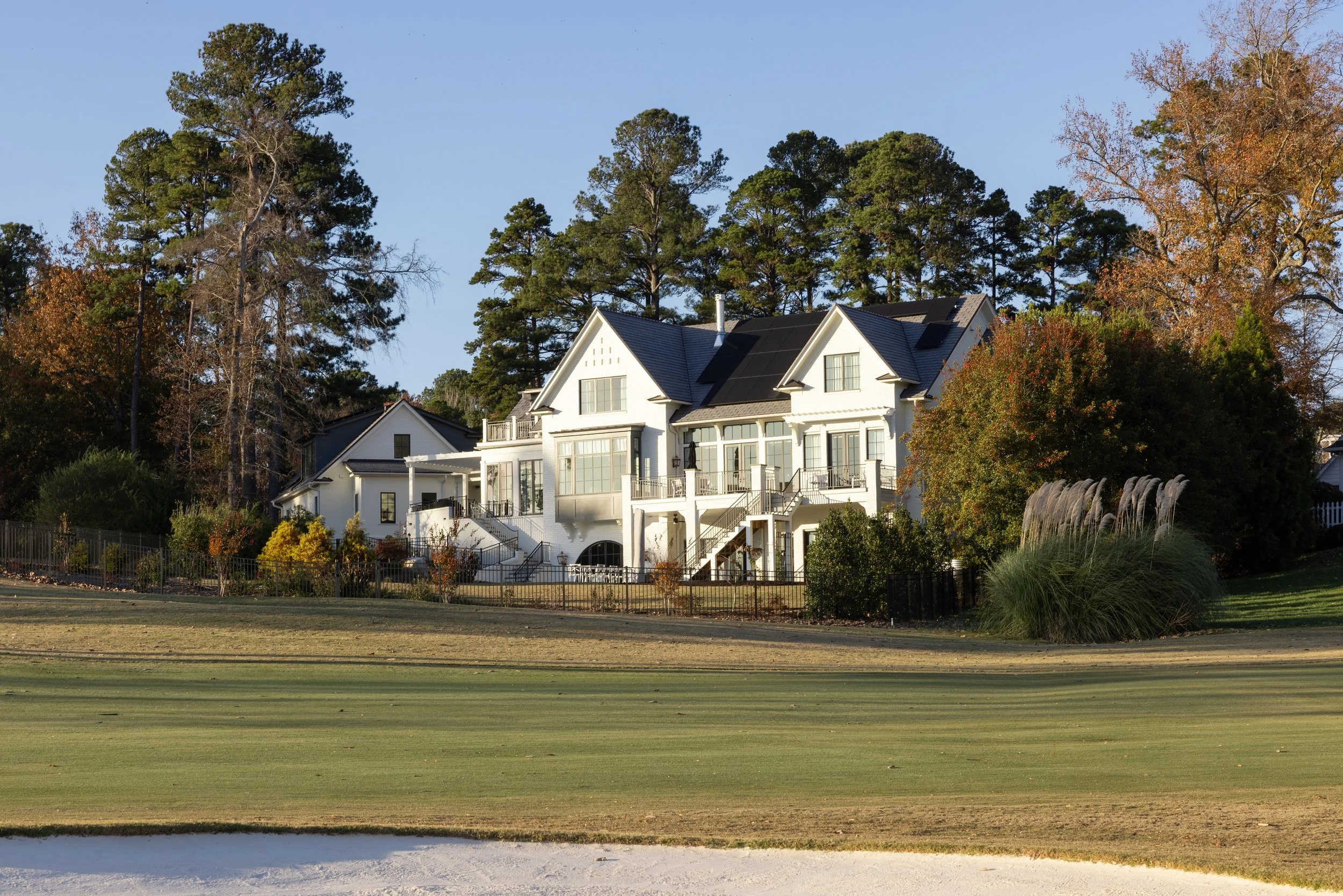 Luxury house with large windows and multiple balconies surrounded by trees and a landscaped yard, view from a golf course.