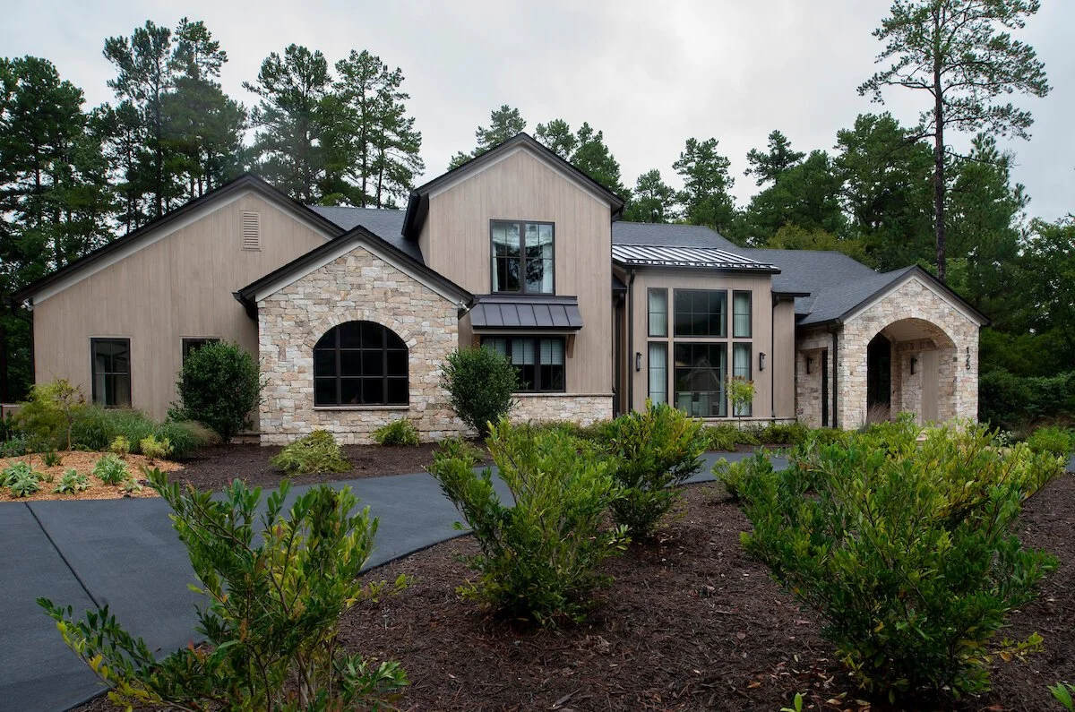 Modern European-inspired luxury estate home in the Triangle featuring natural stone masonry, warm vertical siding, black-framed windows, layered rooflines, and landscaped grounds designed around privacy, land, and timeless architecture.