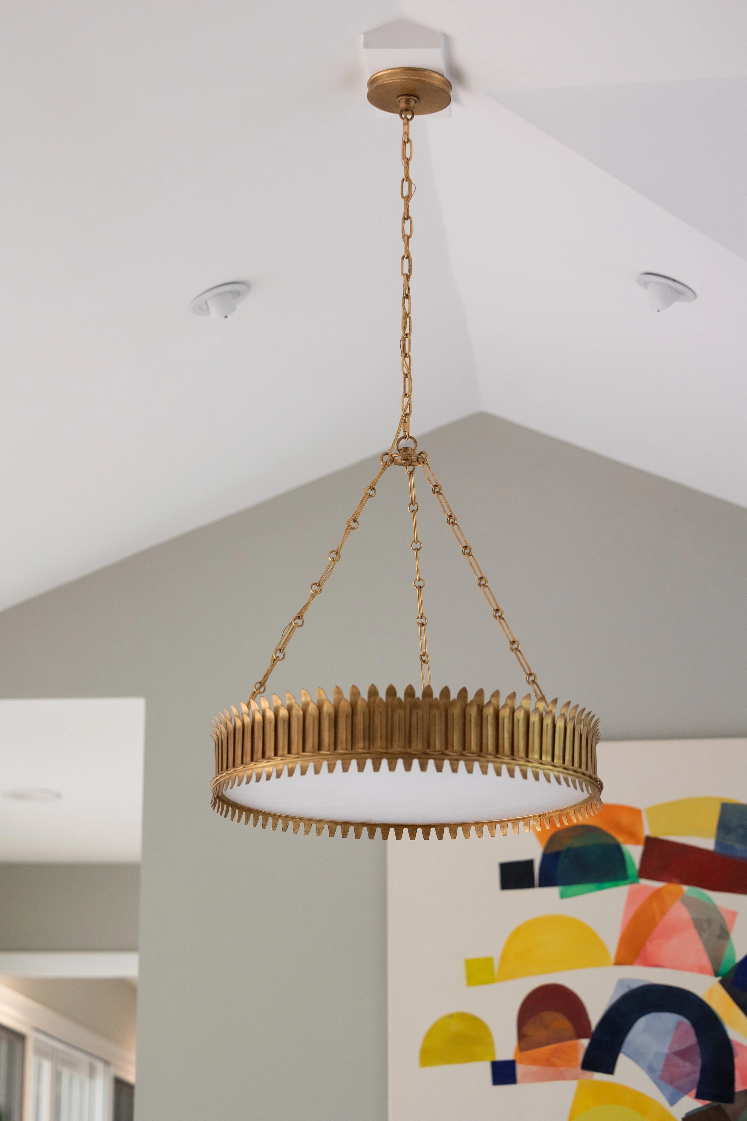 A circular chandelier with wooden teeth-like design hanging from a gold chain in a modern living space.