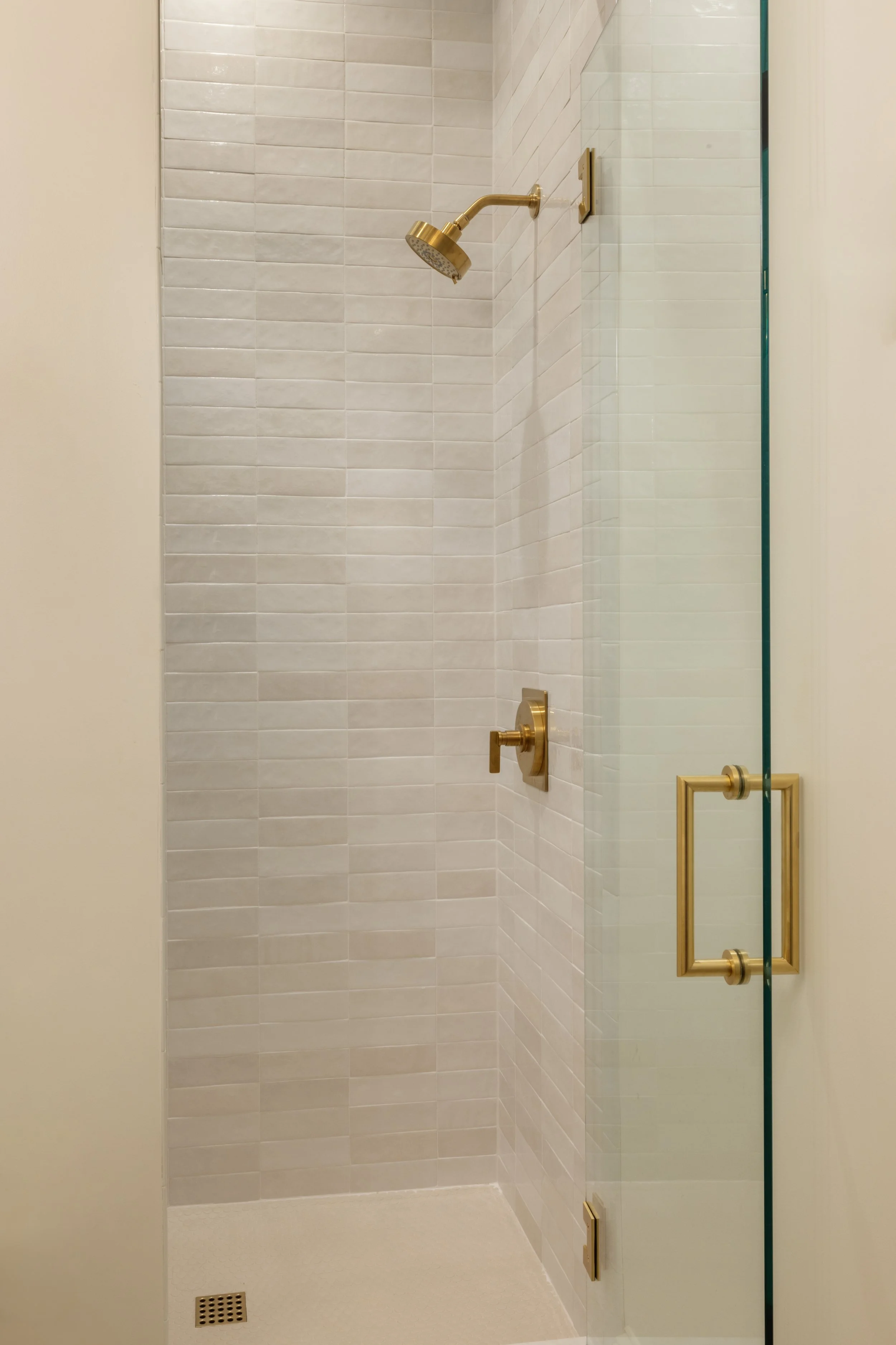 Modern shower with gold fixtures, a glass door, and tiled walls.